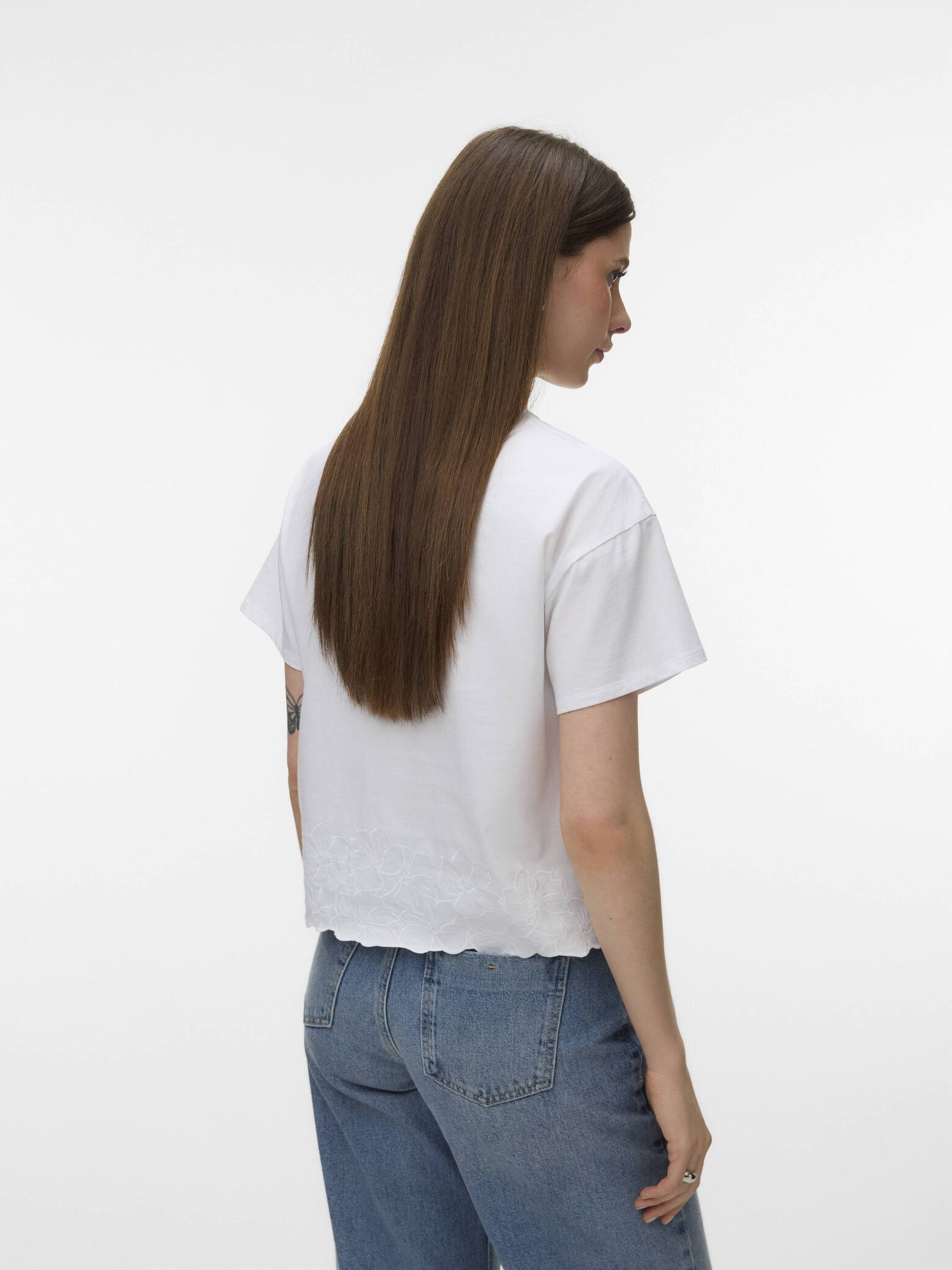 Back view of Vero Moda Noah Embroidered Short Sleeve Top in white with subtle embroidery paired with blue jeans.