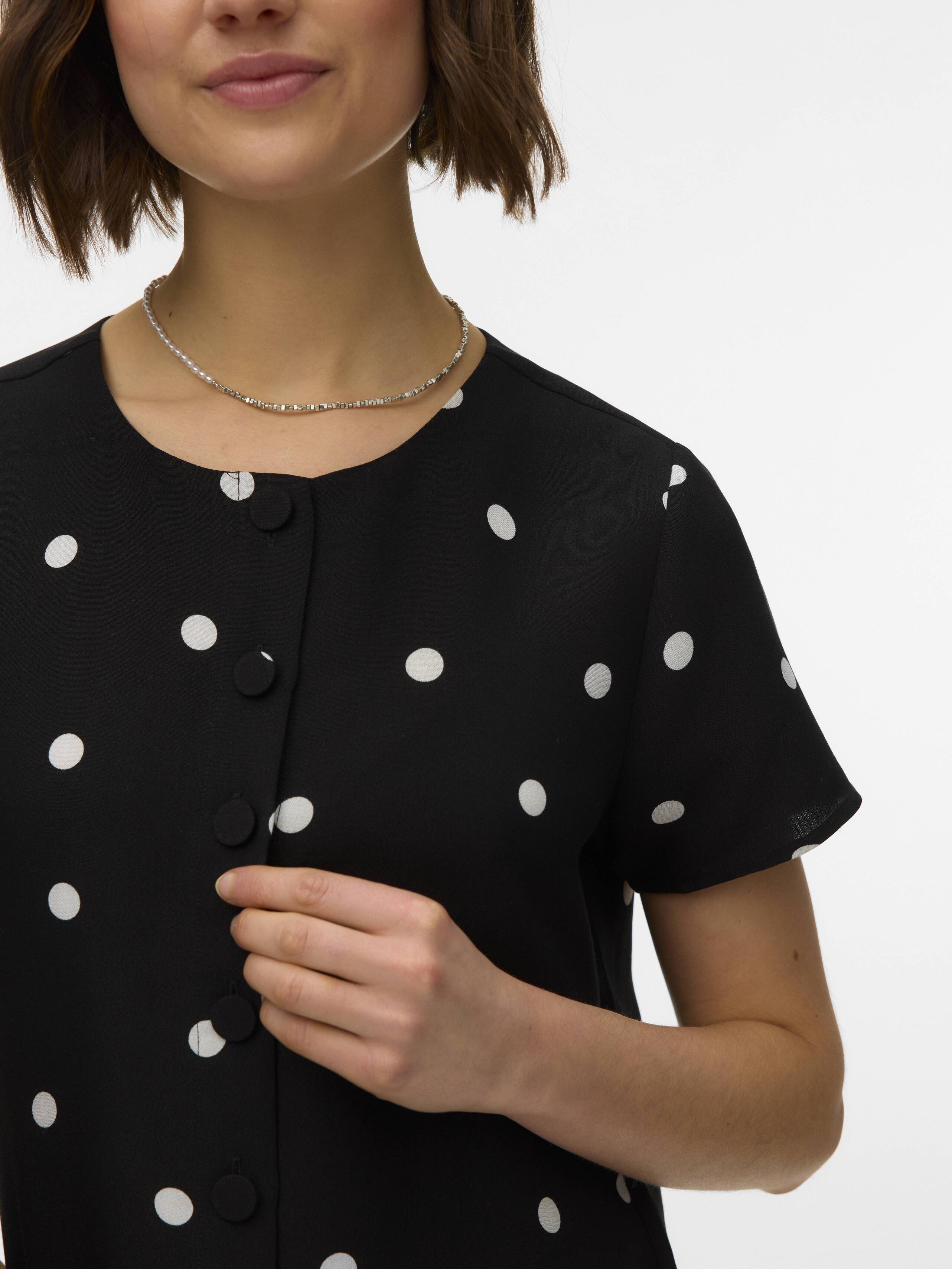 Close-up of a black short-sleeve blouse with white polka dots and fabric-covered buttons worn with a silver necklace.