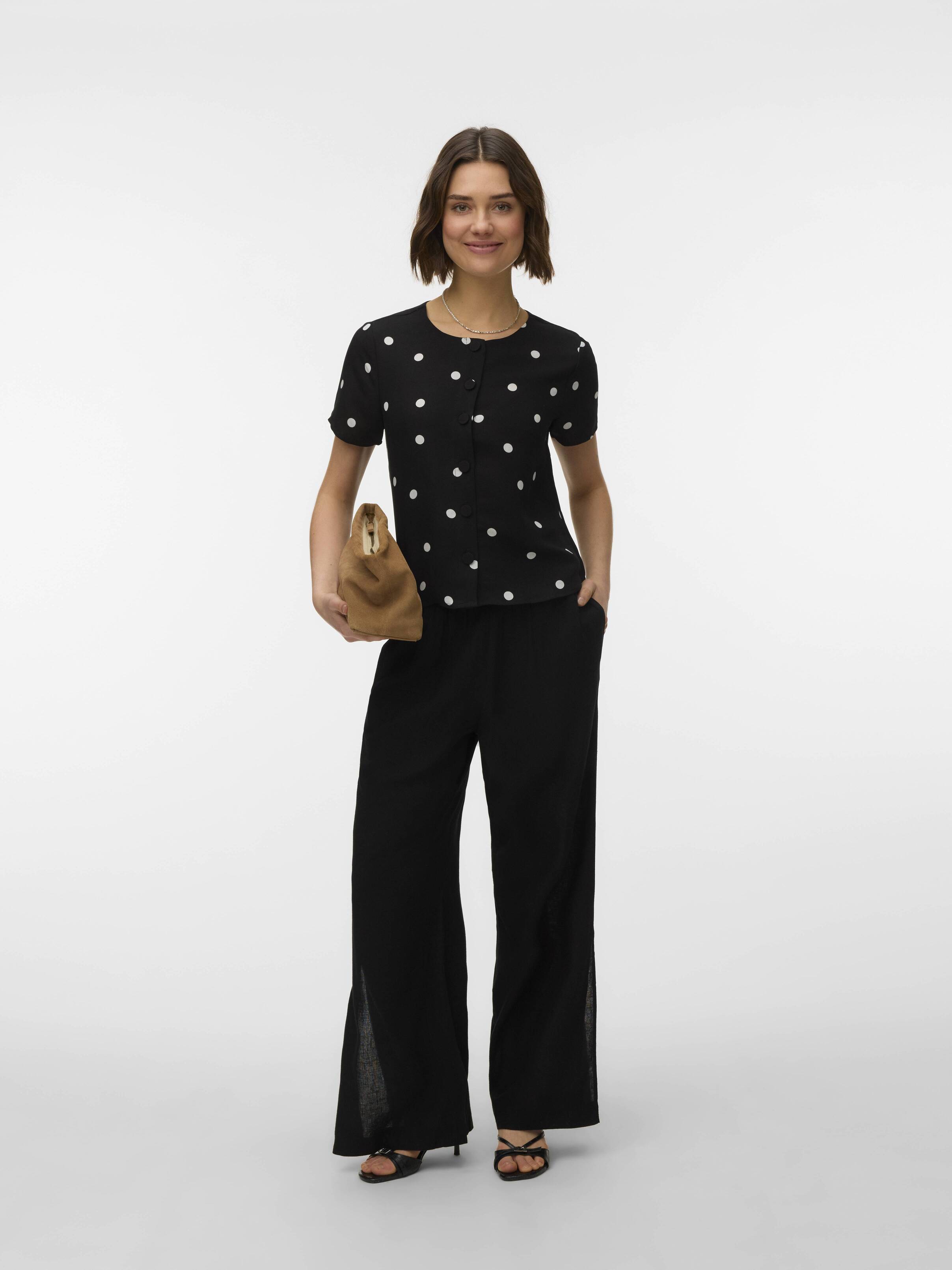 Casual outfit with black polka dot short-sleeve top, wide-leg black pants, sandals, and a small brown handbag.