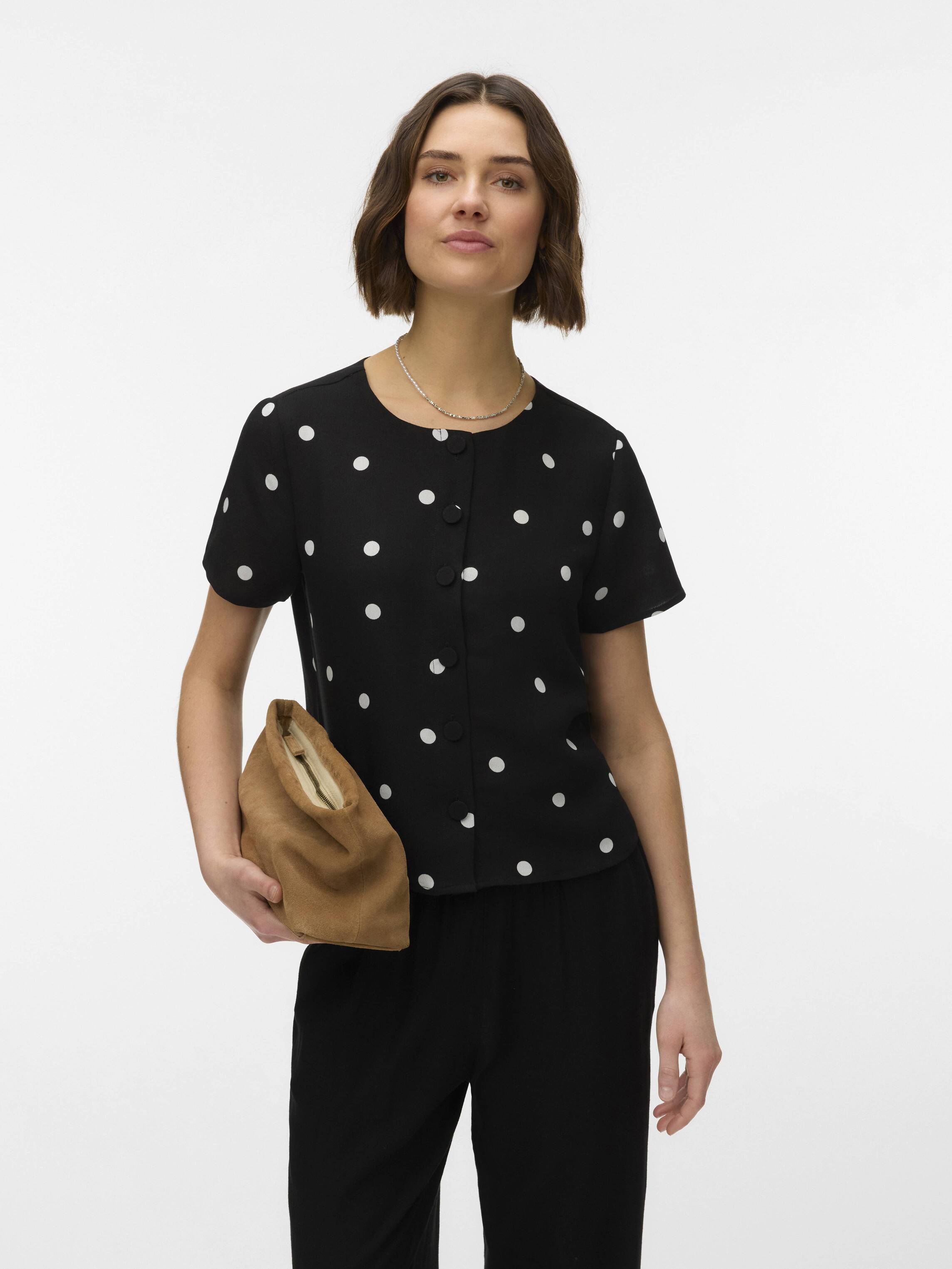 Vero Moda Marianne Short Sleeve Printed Tee in black with white polka dots, styled with a brown clutch and black pants