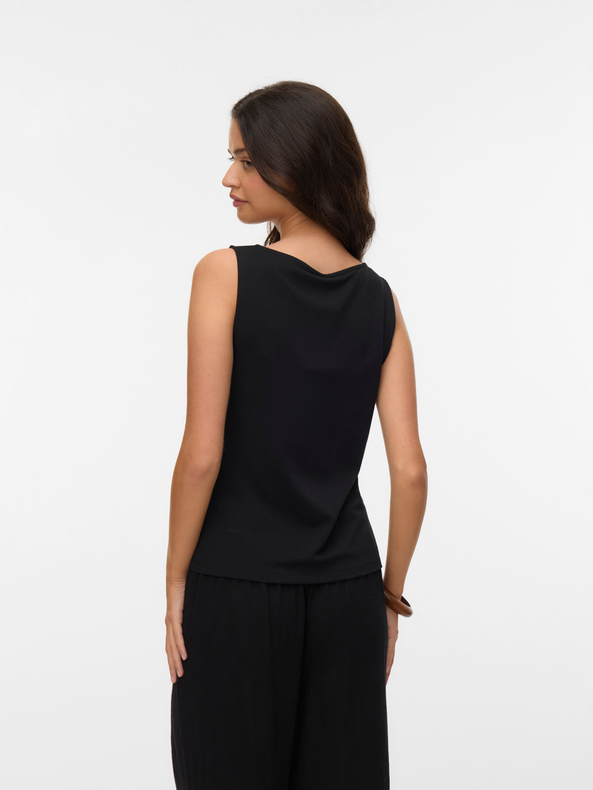 Person wearing a sleeveless black top and loose black pants, shown from the back against a white background