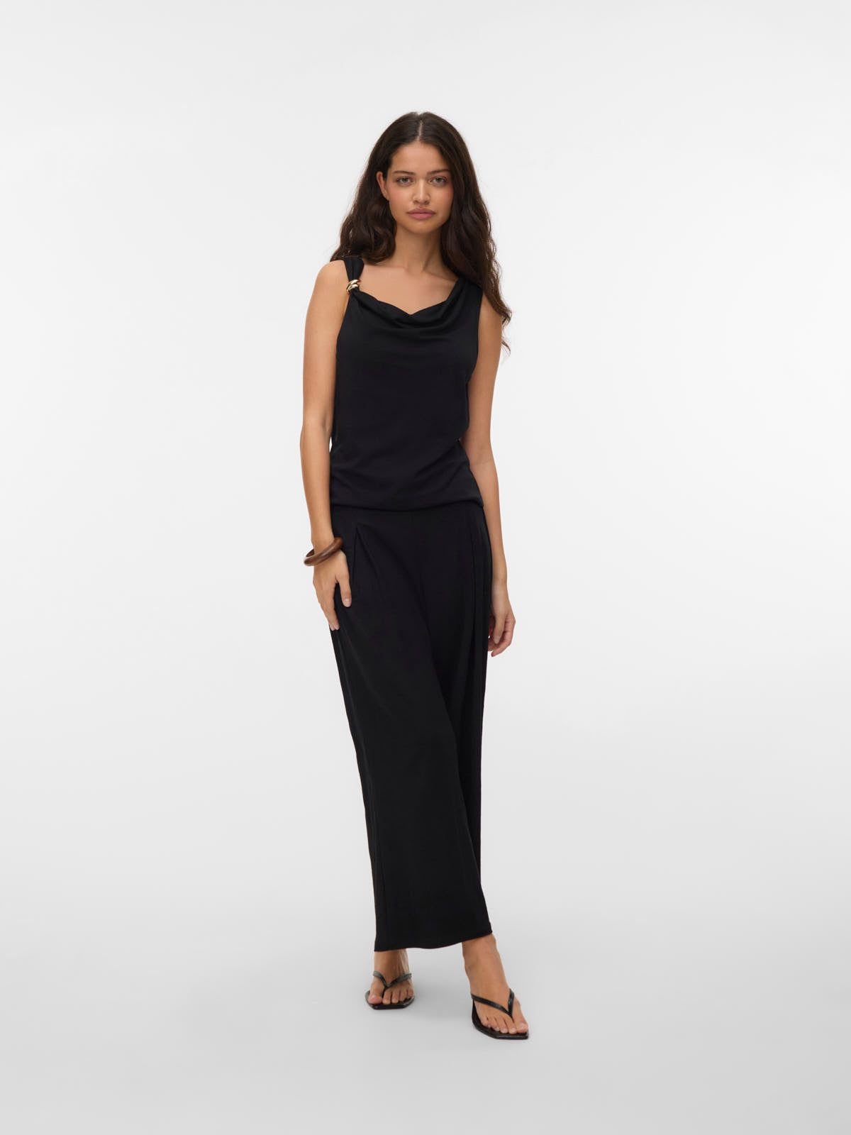 Model in a black sleeveless top with ring detail and matching wide-leg pants against a plain background