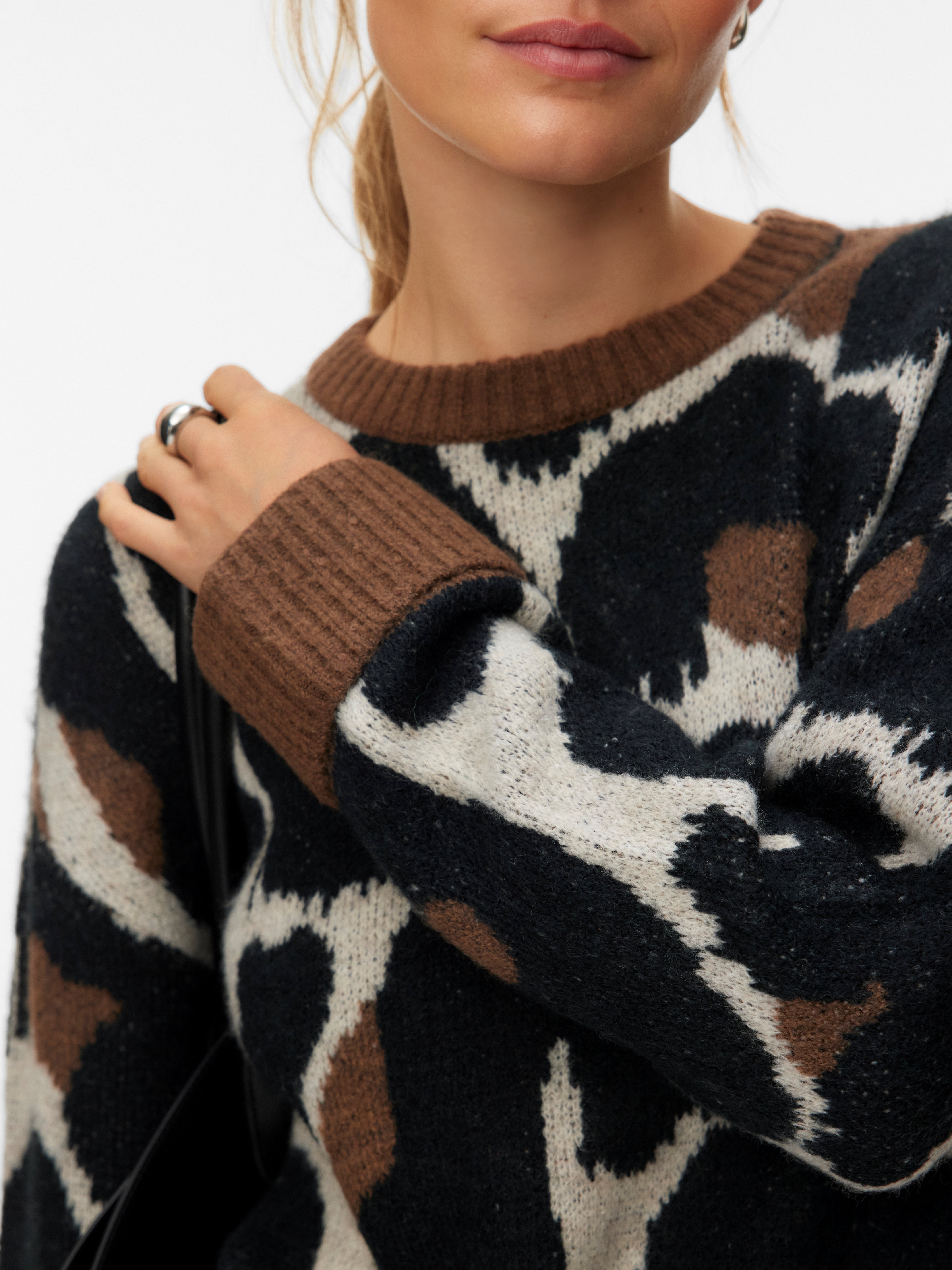 Close-up of a knitted sweater with a brown, black, and cream abstract pattern and ribbed neckline and cuffs.