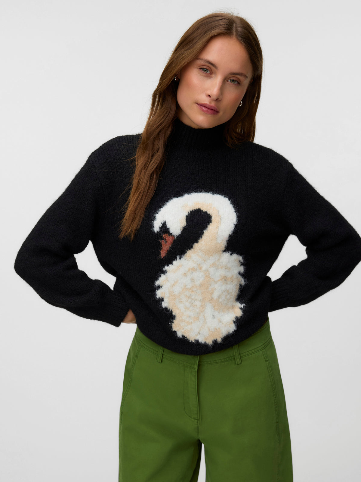 Black turtleneck sweater with a swan motif and green trousers