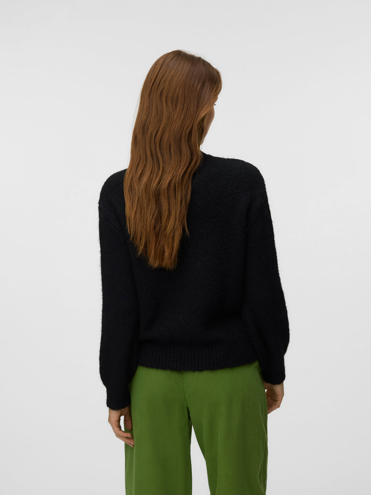 Rear view of a long-haired figure in a black sweater and green trousers