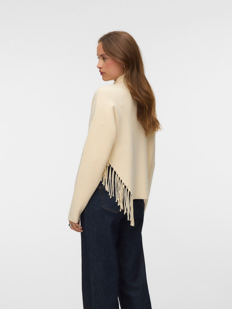 Cream sweater with long fringe paired with dark denim jeans, shown from the side.