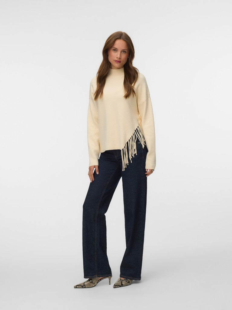 Fashion model in a cream fringe sweater, dark blue wide leg jeans, and pointed heels against a light background