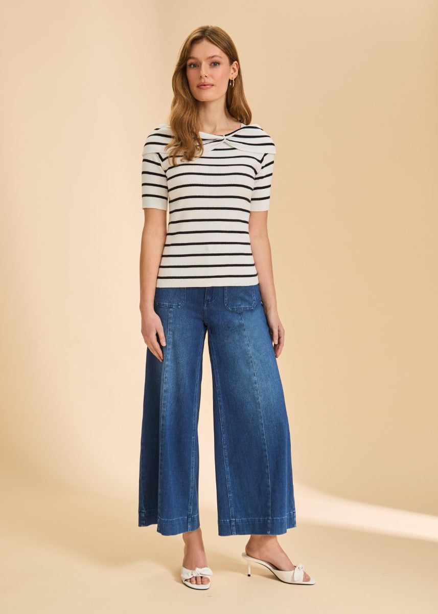 Person in a white and black striped short-sleeve top paired with wide-leg blue denim pants and white heeled sandals.