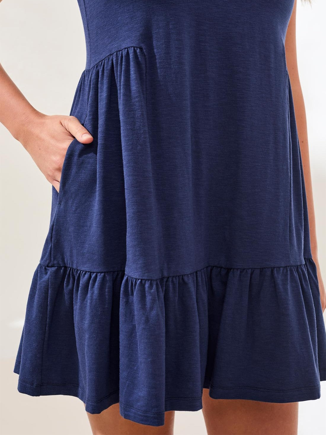 Close-up of a navy blue tiered dress with a pocket and gathered fabric details on light background.