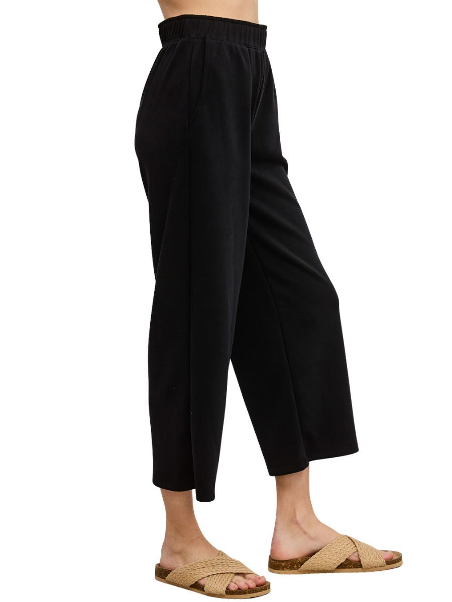 Black wide-leg cropped pants with elastic waistband paired with woven sandals on light background