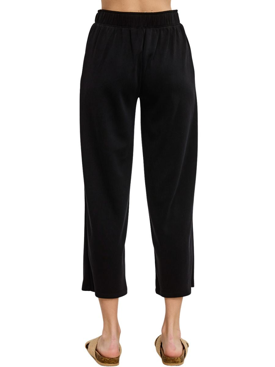 Black cropped trousers with an elastic waistband and straight legs paired with casual slip-on sandals