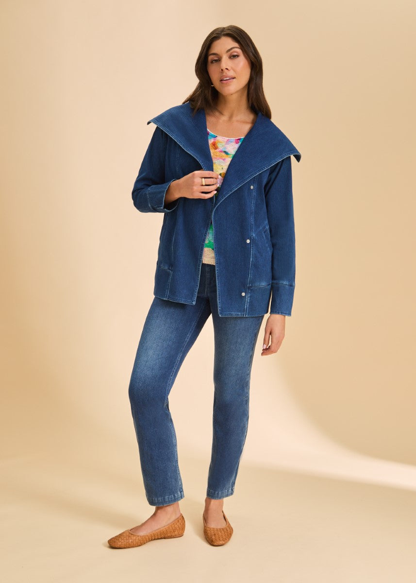 Person standing in blue denim jacket with wide collar, blue jeans, colorful top, and brown woven flats on beige background