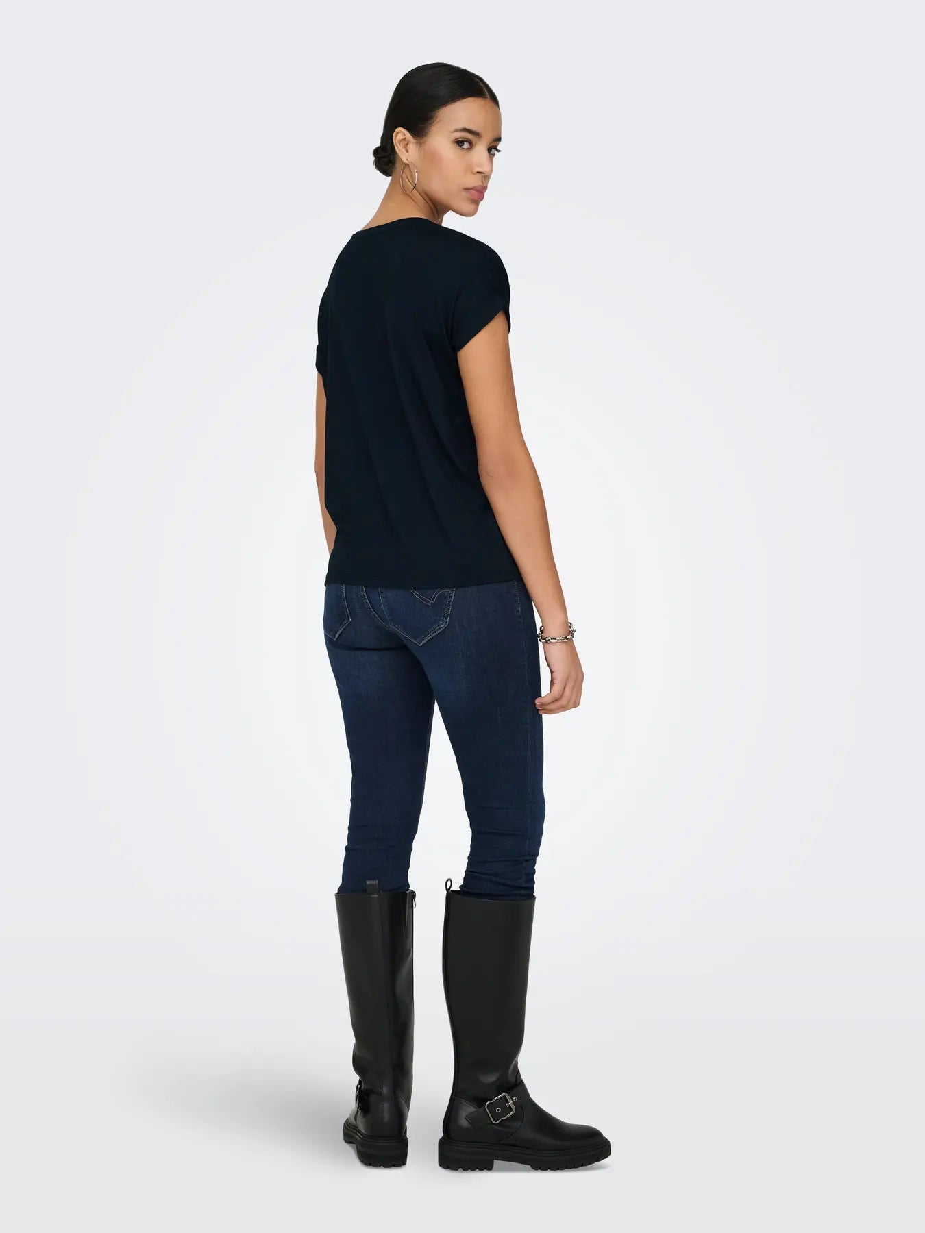 Back view of a person wearing a black short-sleeve top, dark blue denim jeans, and knee-high black boots.
