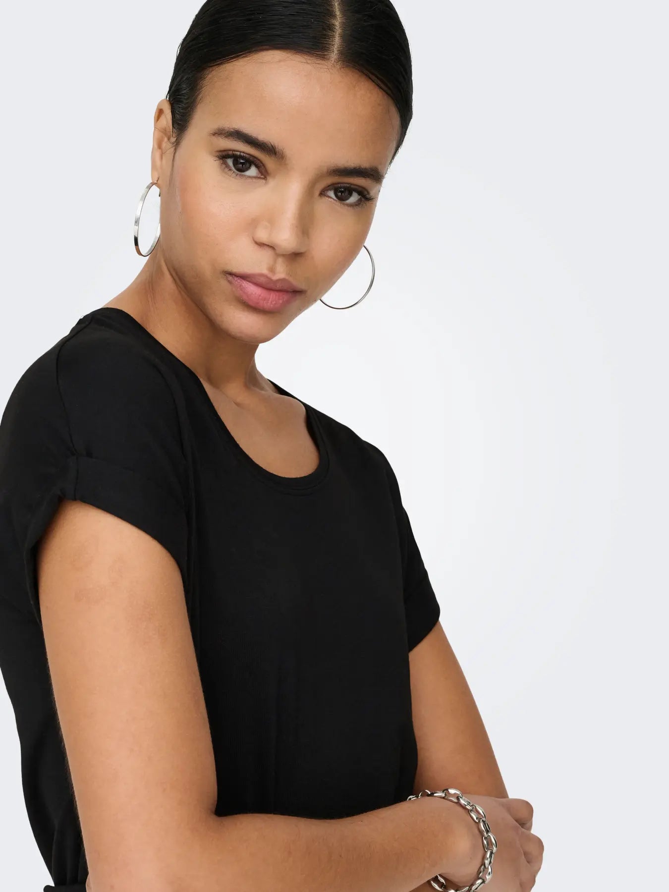 Close-up of a person wearing a black short-sleeve top with silver hoop earrings and a silver chain bracelet.
