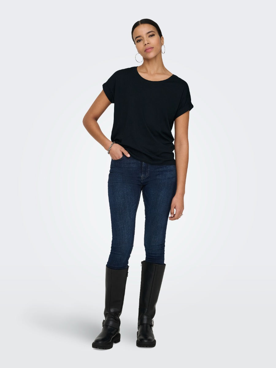 Person in a black short-sleeve top, dark skinny jeans, and black knee-high boots against a plain background.