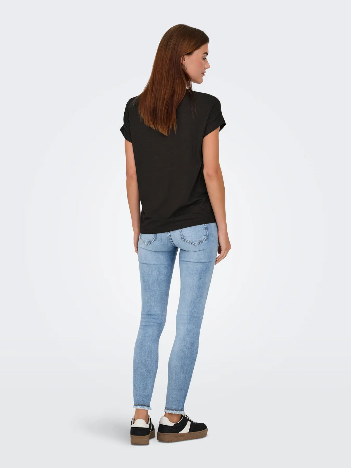 Back view of a person in a black short-sleeve shirt, light blue denim jeans, and black and white sneakers.