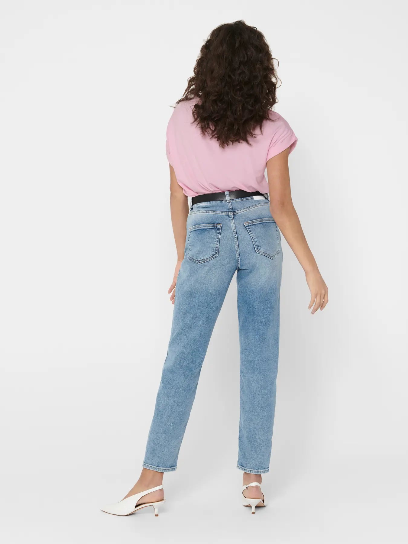 Rear view of light blue denim jeans paired with a pink short-sleeve top and white slingback heels on a neutral background.