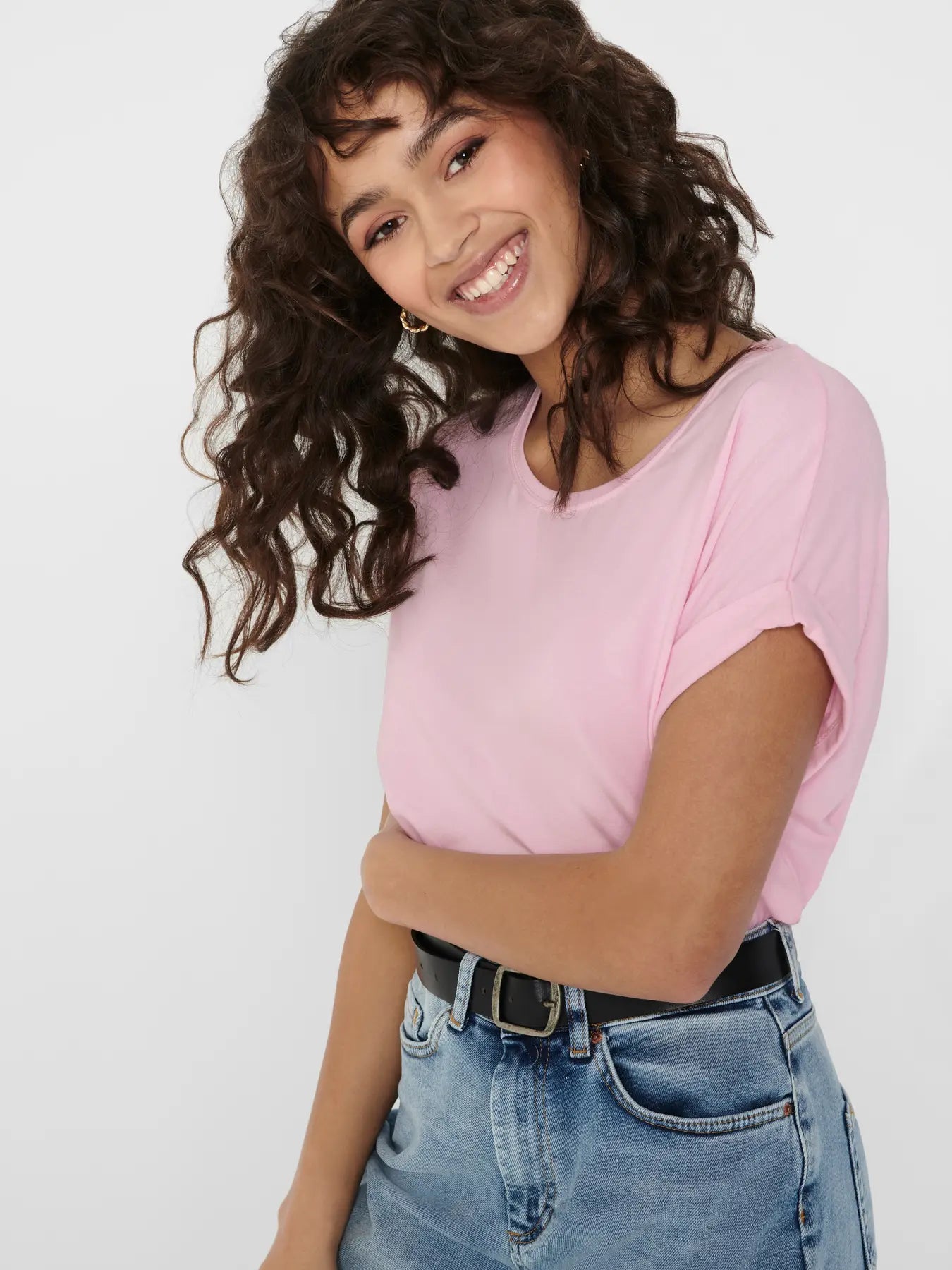 Smiling figure with curly hair wearing a light pink short-sleeve top tucked into high-waisted blue denim jeans with a black belt.
