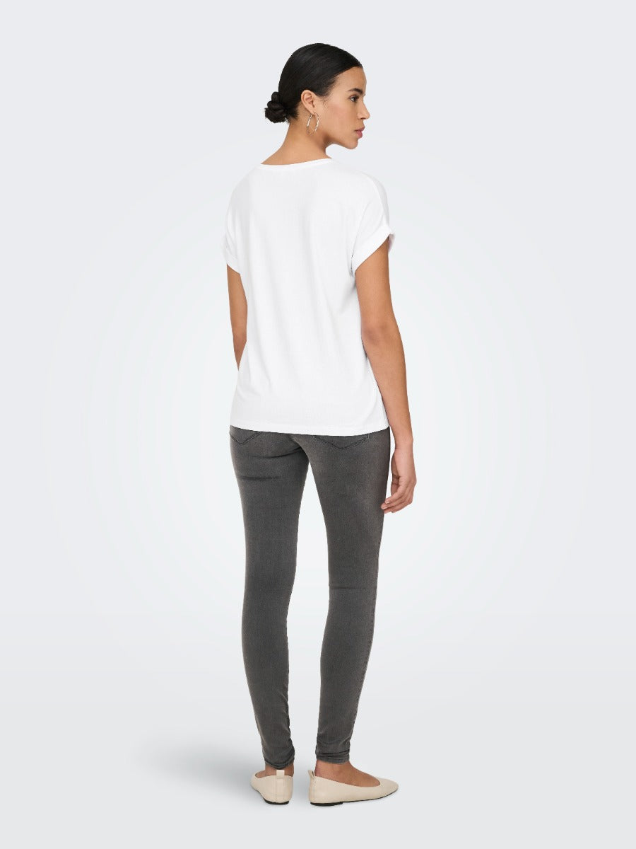 Rear view of a person wearing a white short-sleeve top, dark gray fitted pants, and beige flat shoes against a plain background.