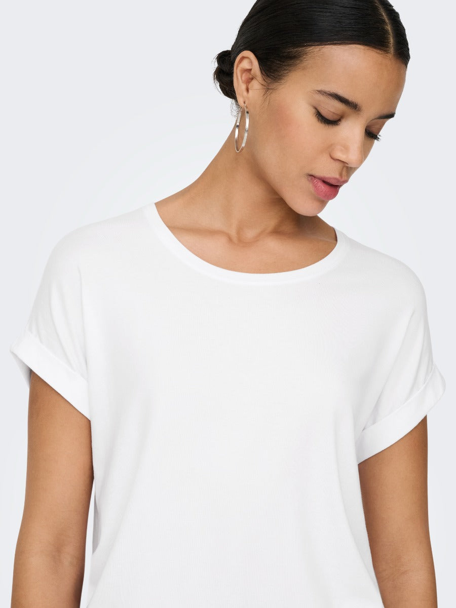 Close-up of a person wearing a plain white short-sleeve top with hoop earrings against a light background.
