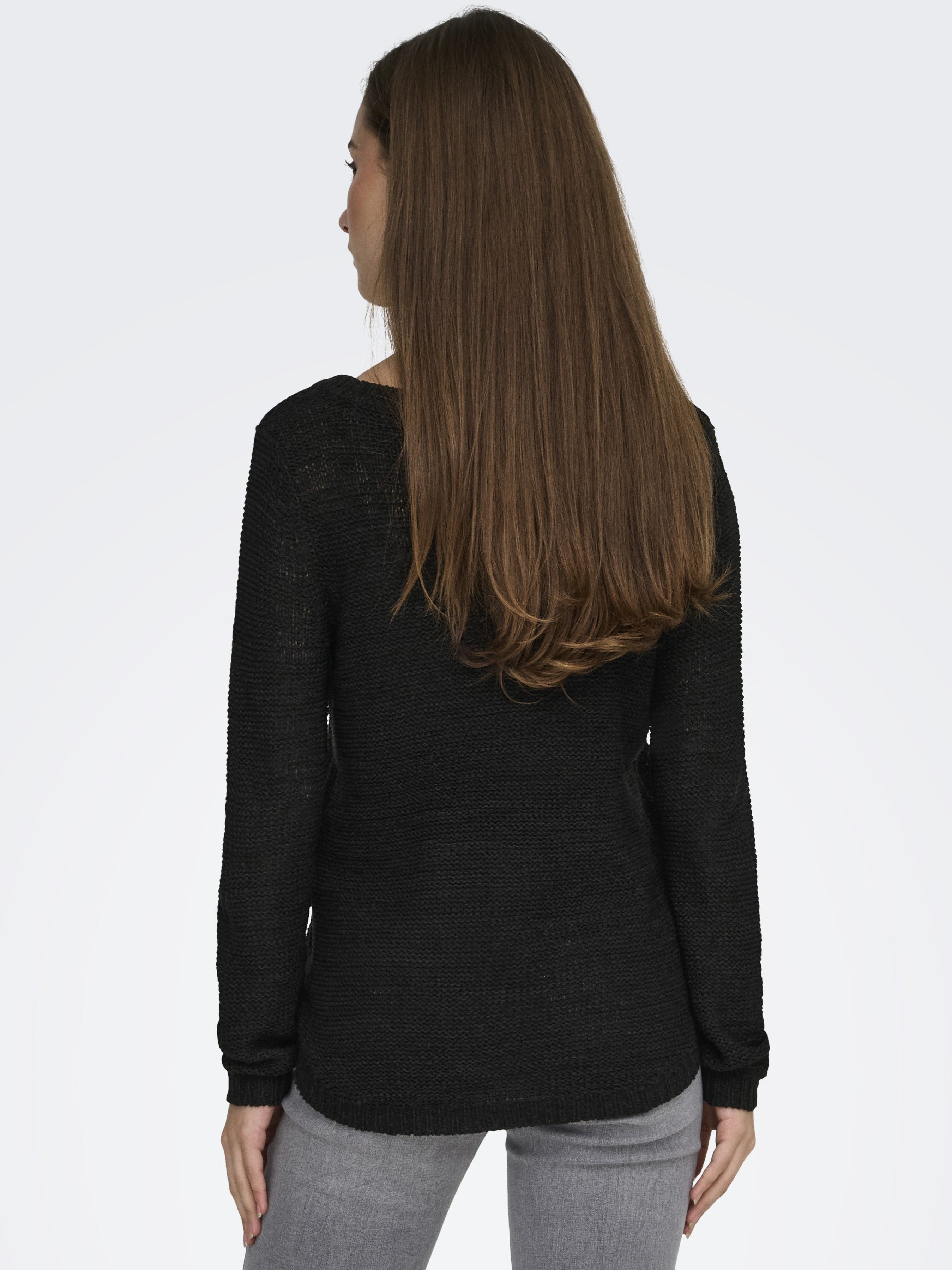 Back view of a black knitted long-sleeve sweater paired with light gray pants against a plain background.
