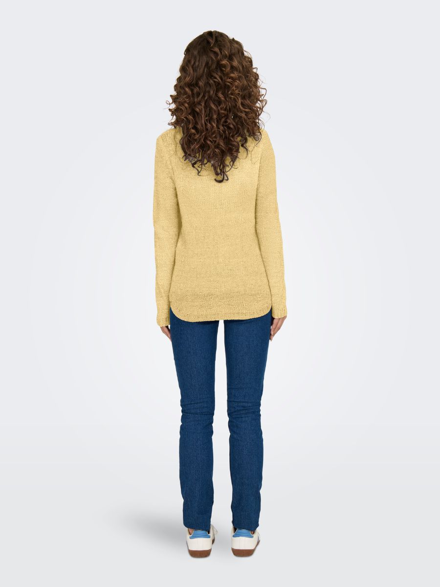 Curly hair from behind, wearing a yellow sweater and blue jeans, standing on a plain light gray background.