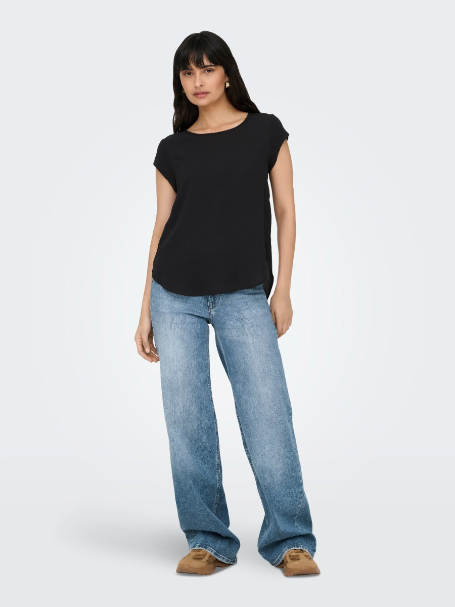Person wearing a black short-sleeve top paired with light blue wide-leg denim jeans and brown shoes.