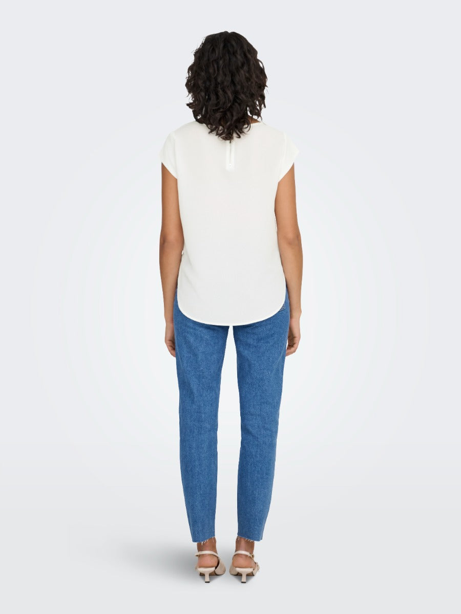 Person with curly hair wearing an off-white short sleeve top and blue denim jeans, standing facing away