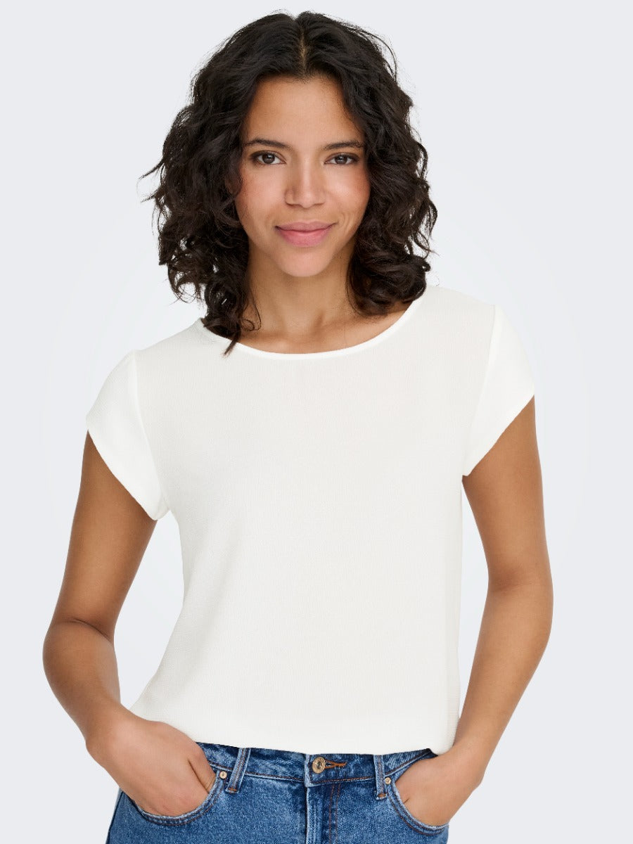 Only Vic Solid Top by Only in off-white, featuring a solid design and classic short sleeves, styled with blue denim jeans
