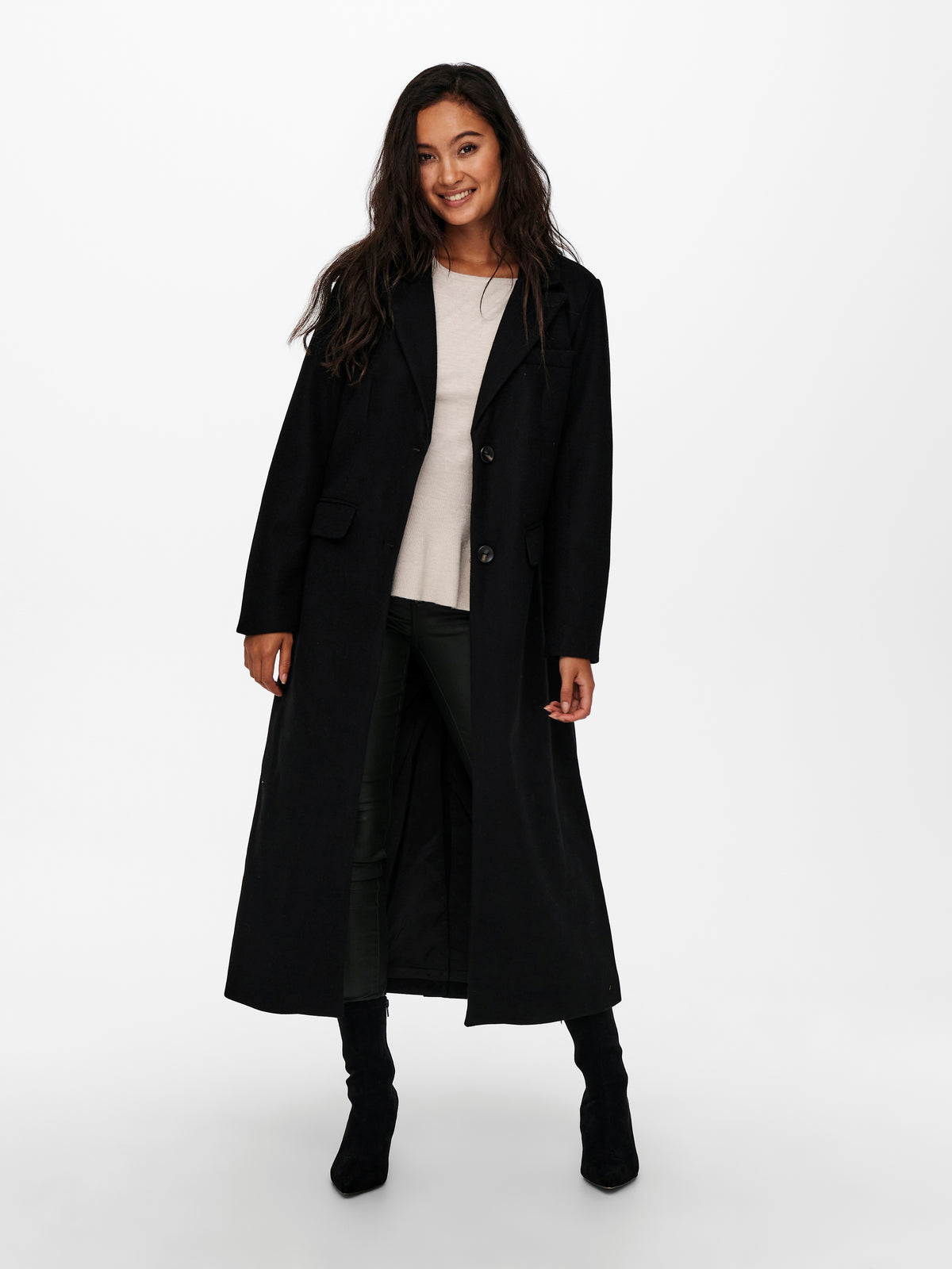 Black long coat over a cream top, dark jeans, and black ankle boots on a white background