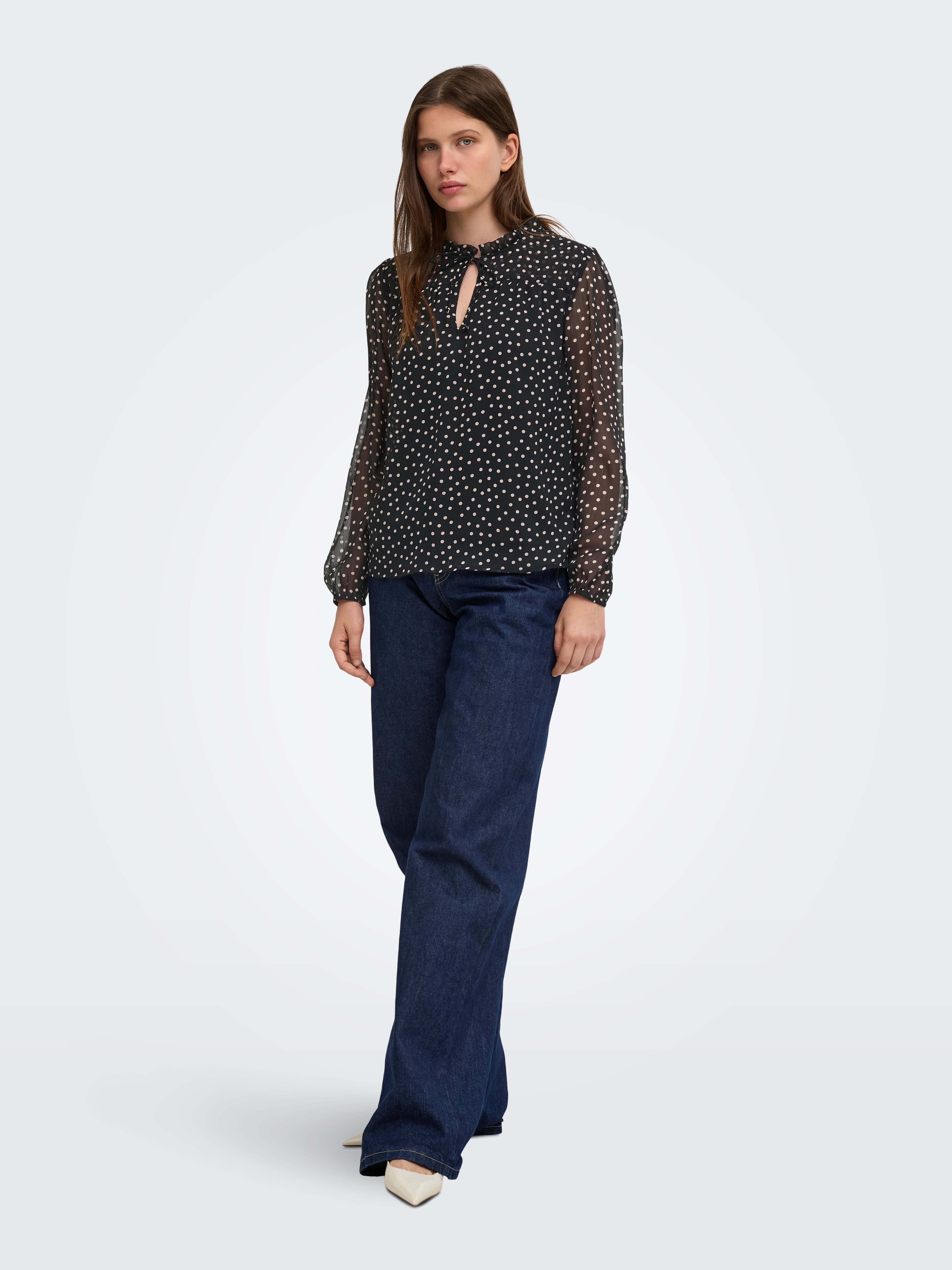 Black sheer long-sleeve top with white polka dots paired with dark blue wide-leg denim pants and white shoes.