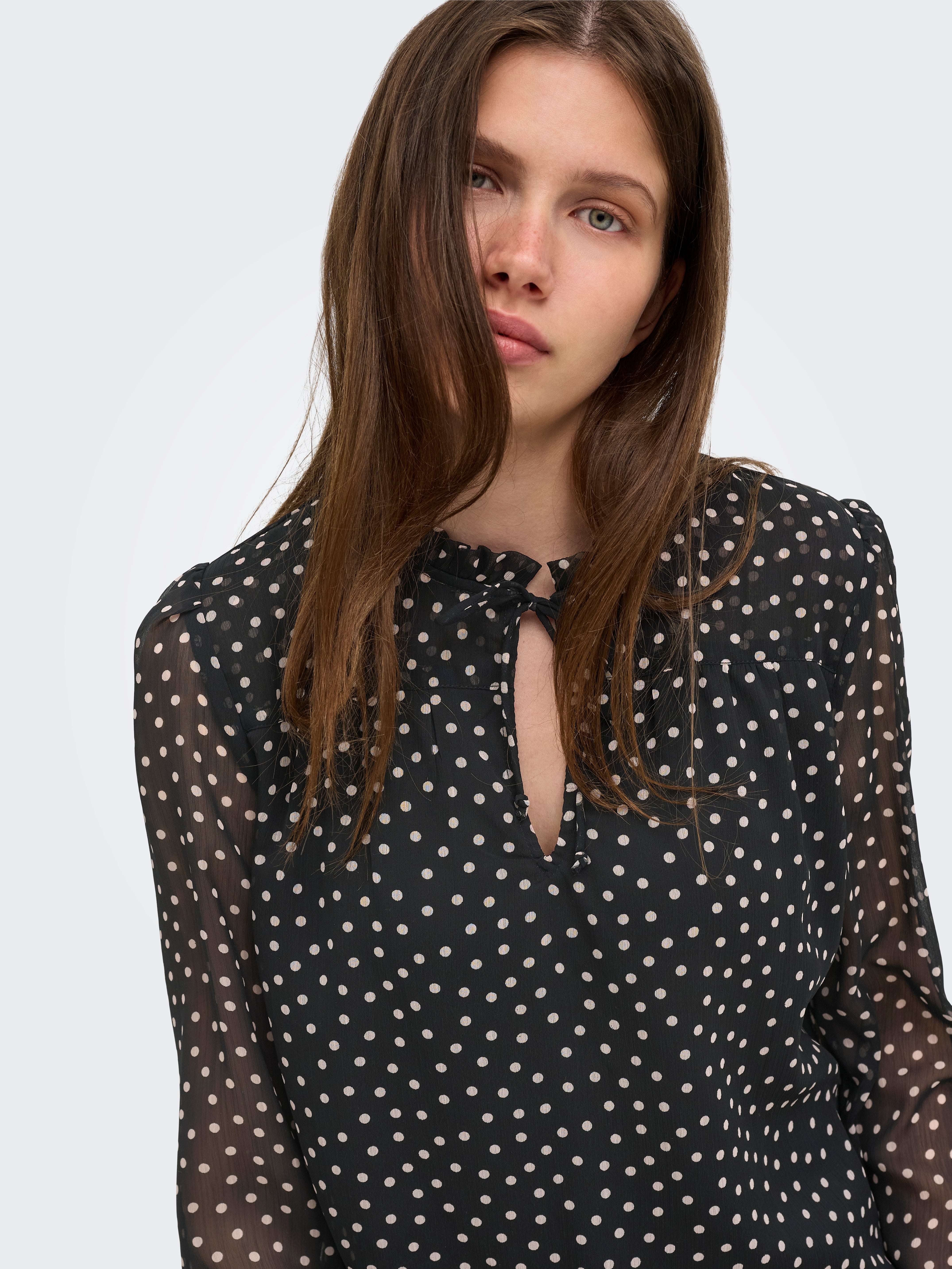 Close-up of a black sheer top with white polka dots and a keyhole neckline with a small tie detail.
