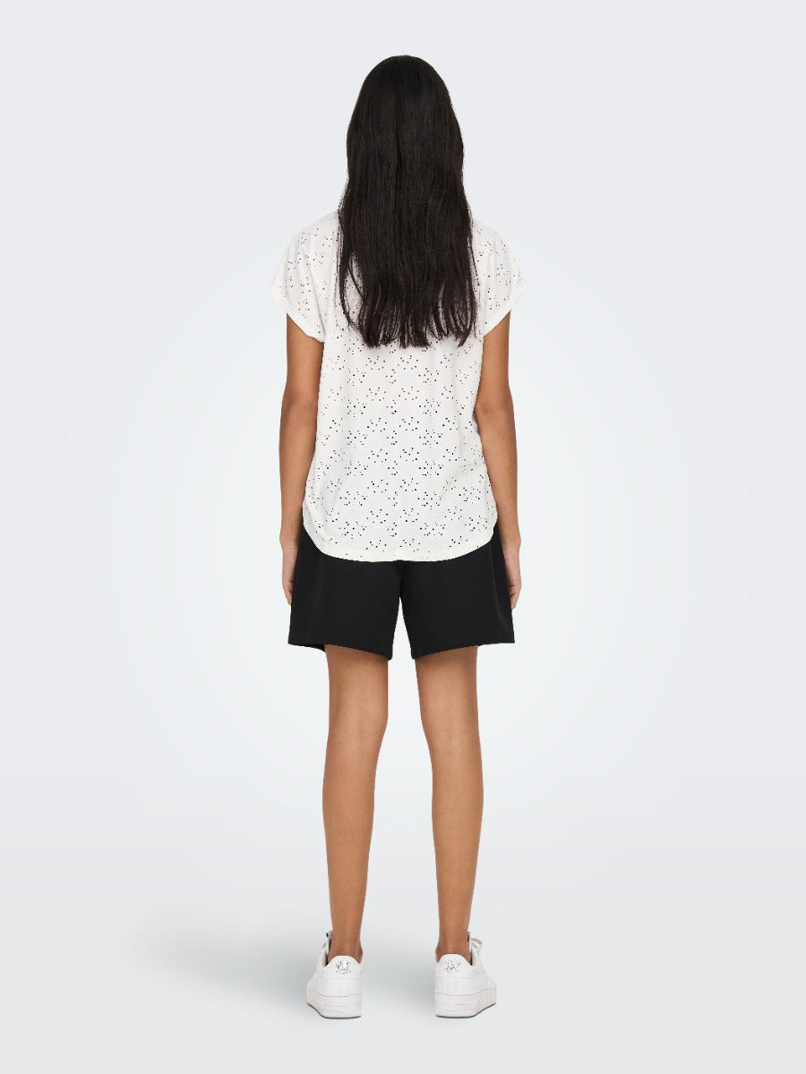 Person with long dark hair wearing a white eyelet top, black shorts, and white sneakers, standing with back to camera.