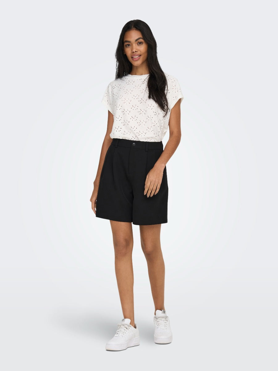 Person wearing a white eyelet short sleeve top paired with black high-waisted shorts and white sneakers