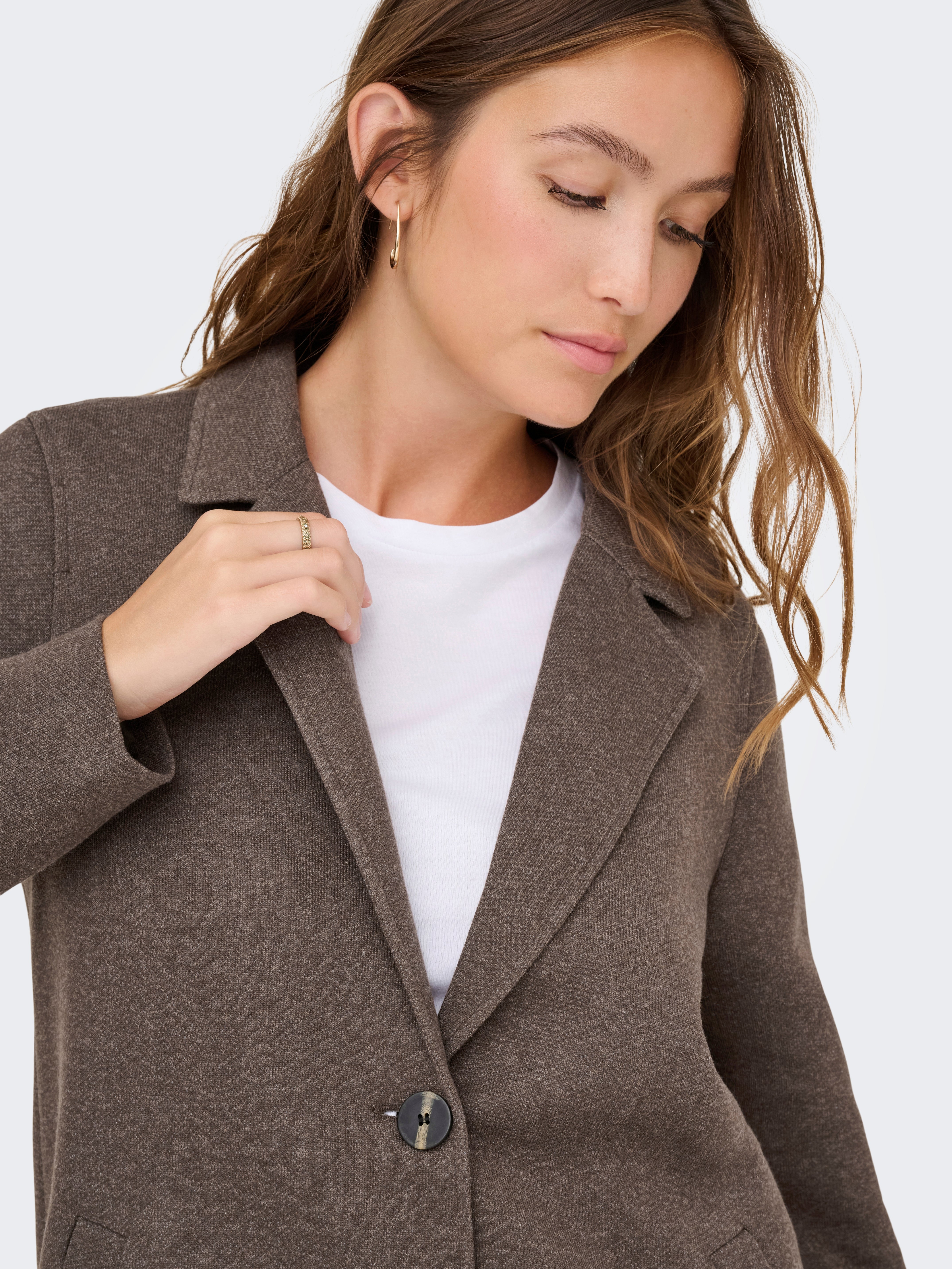Close-up of a brown winter coat with a button, worn over a white top, featuring subtle texture and a notch collar.