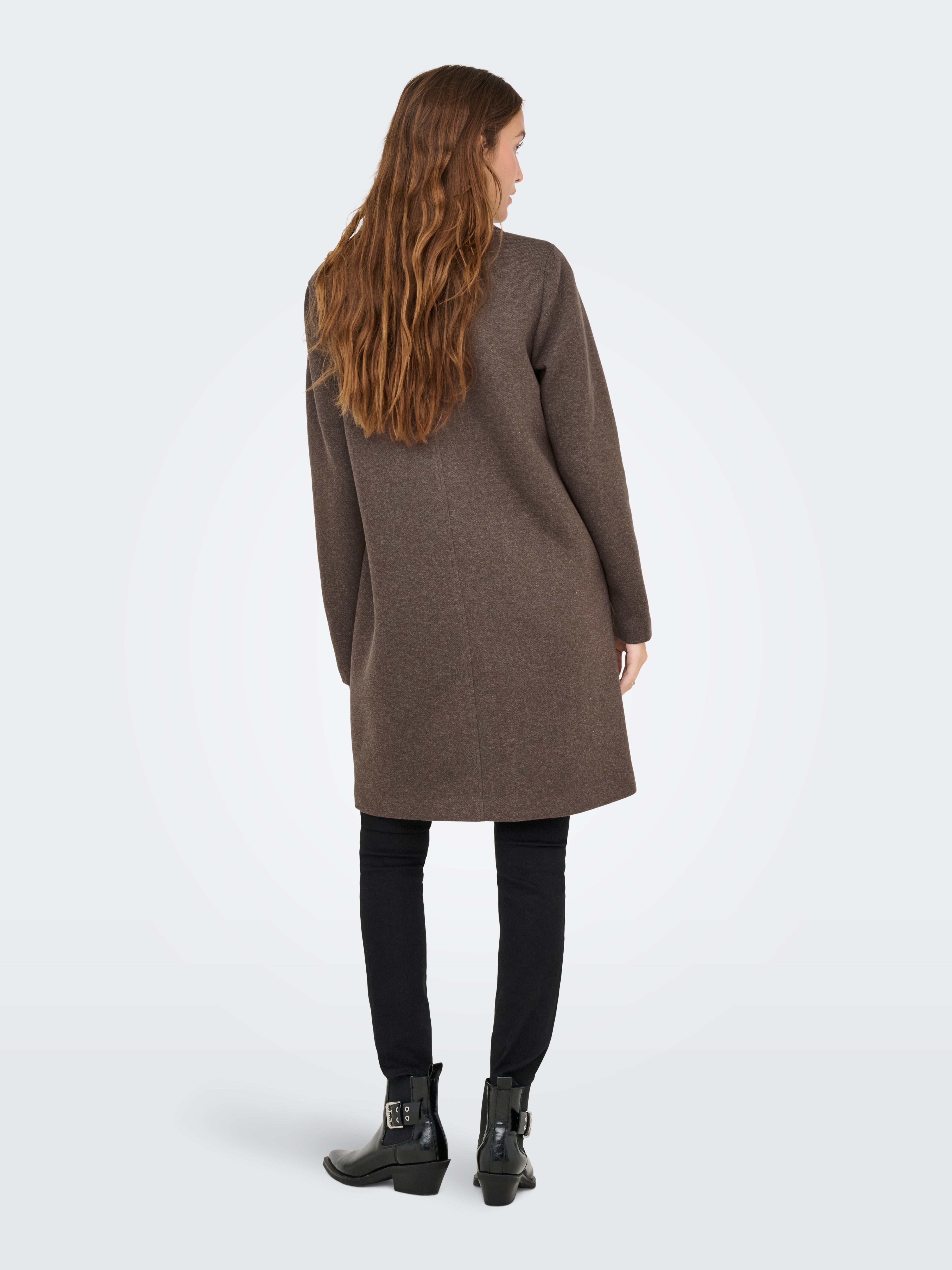 Back view of a long brown coat paired with black pants and black ankle boots on a light background.
