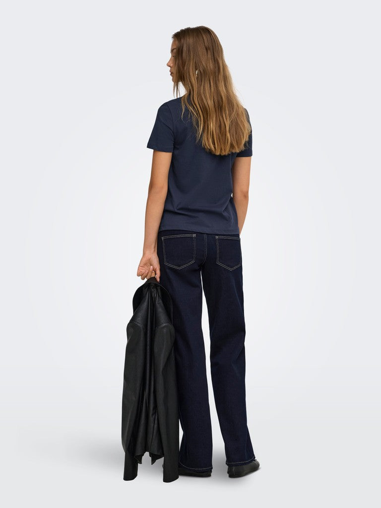 Back view of a model in a navy top and dark denim jeans holding a black jacket