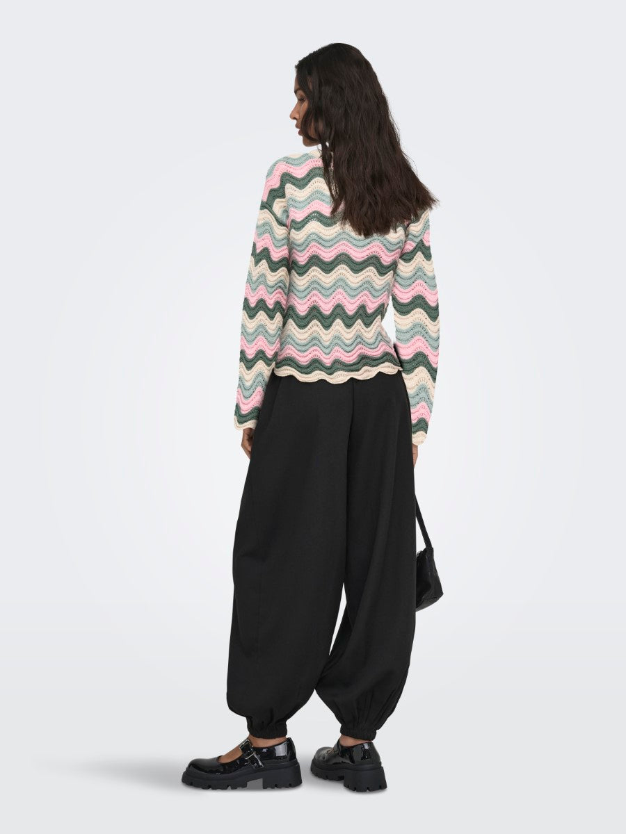 Person seen from behind wearing a pastel wavy striped sweater with loose black pants and black shoes, holding a small bag.