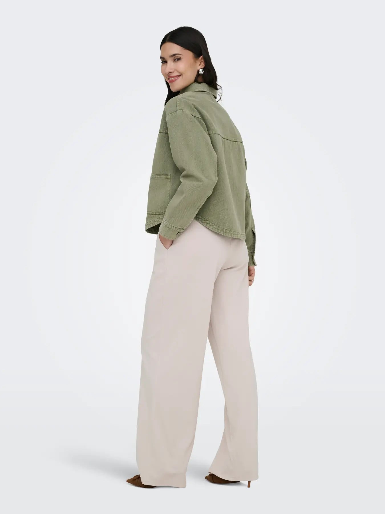 Back view of a person wearing an olive green jacket and wide-leg cream-colored trousers against a white background.