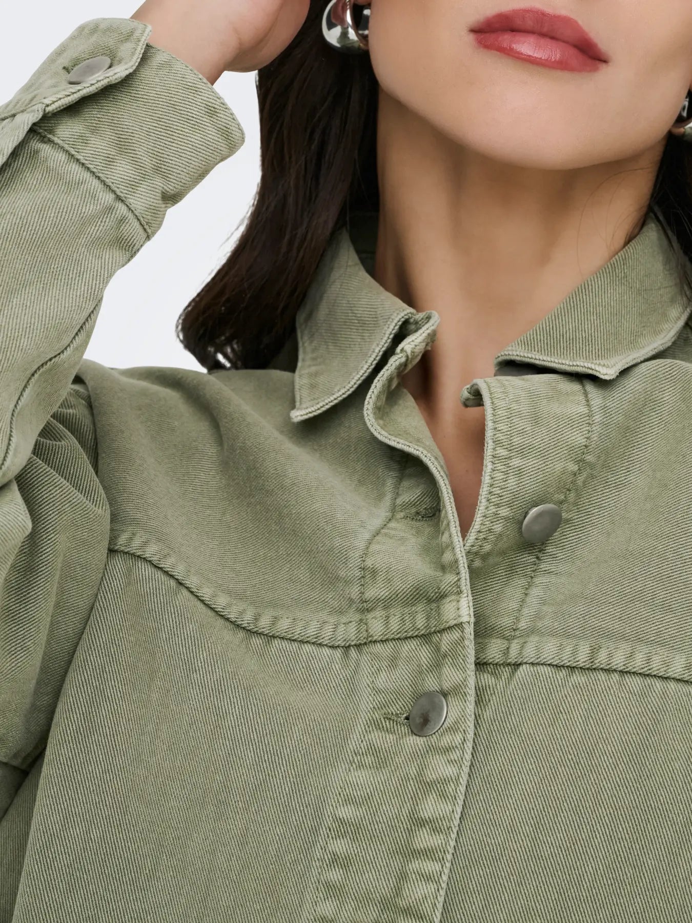 Close-up of sage green denim jacket with metal snap buttons and raised collar detail