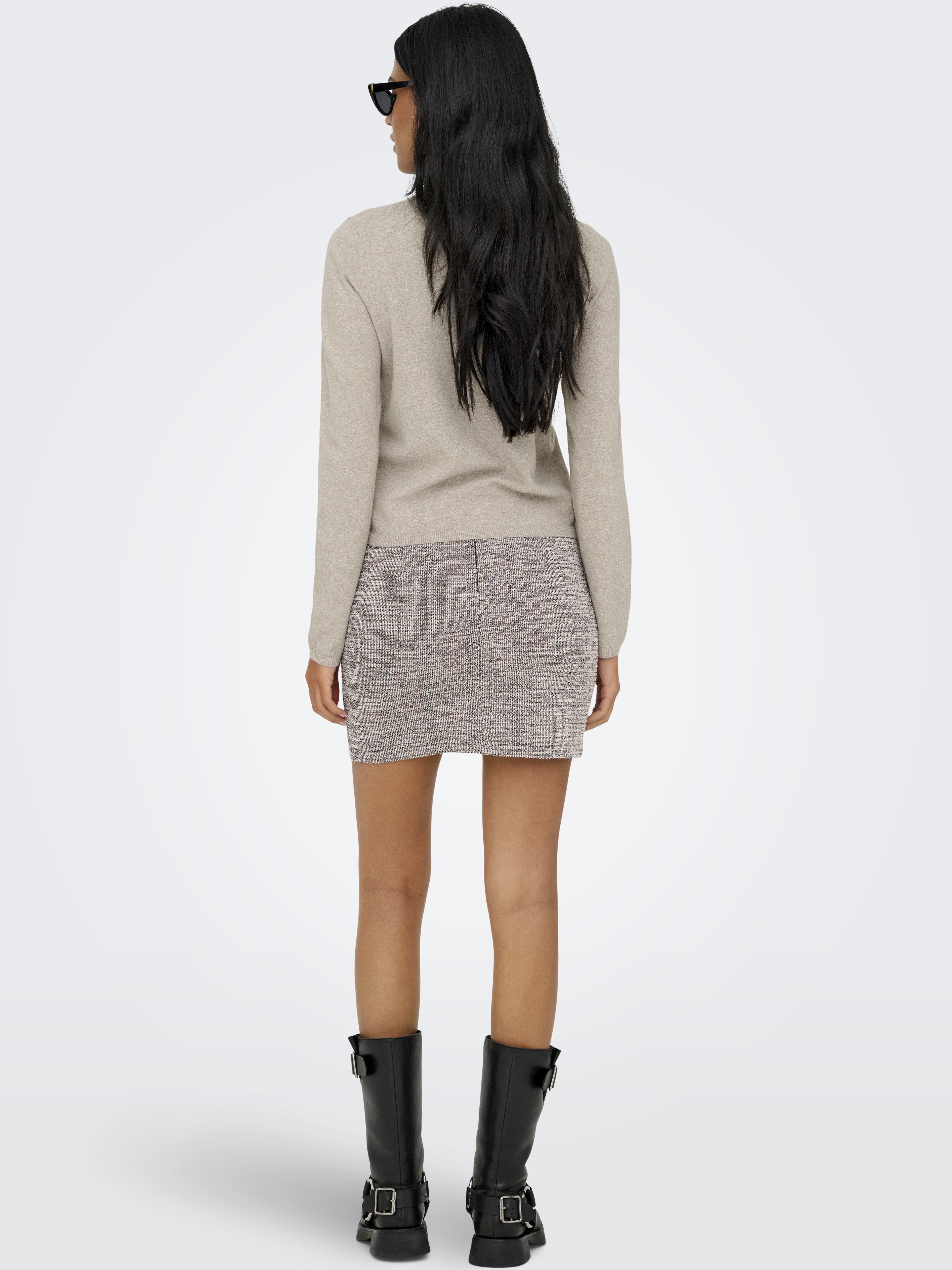 Back view of a beige long-sleeve sweater paired with a textured neutral mini skirt and black mid-calf boots.