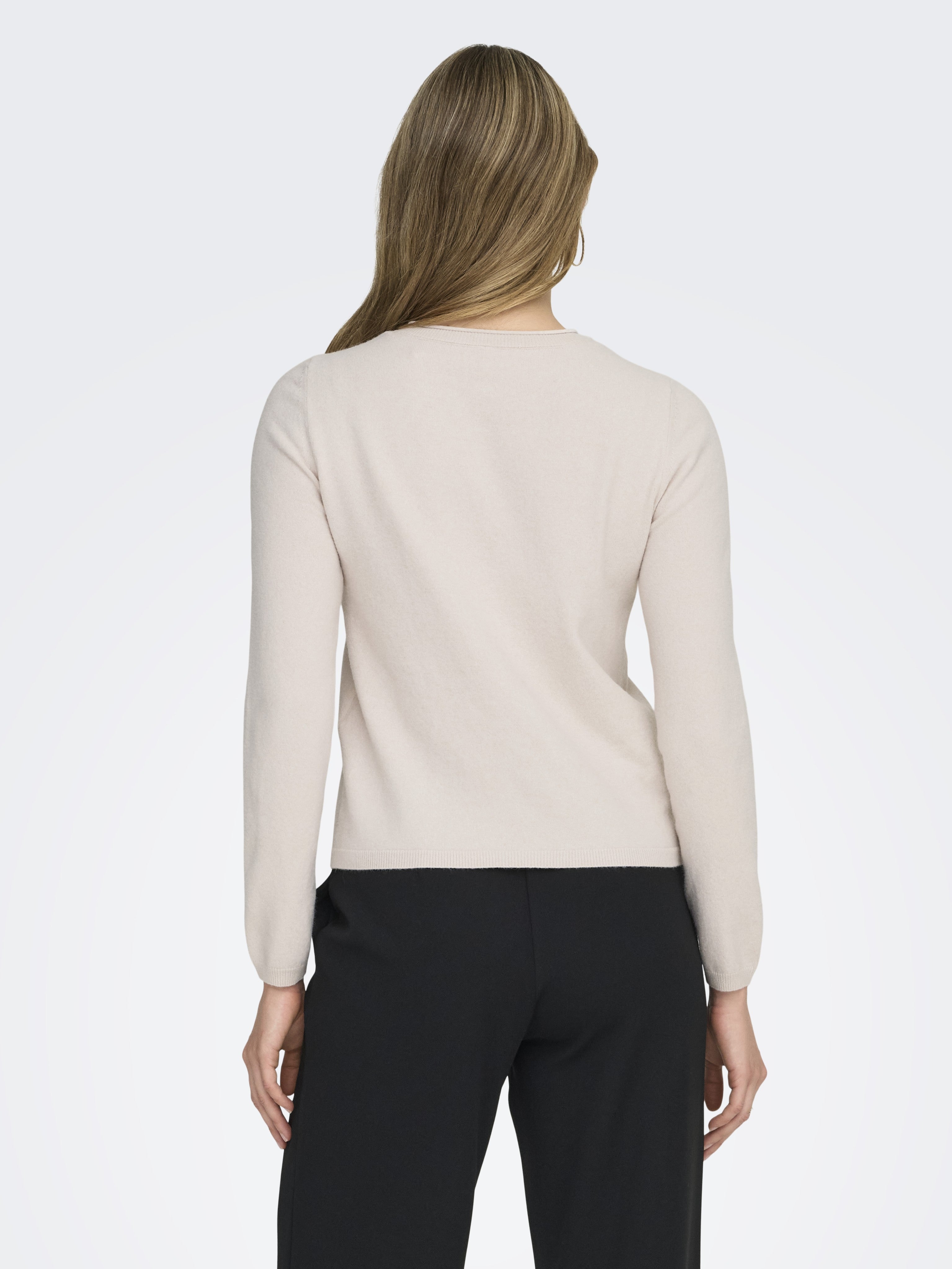 Back view of a light beige long-sleeve knit sweater paired with black trousers against a plain background.