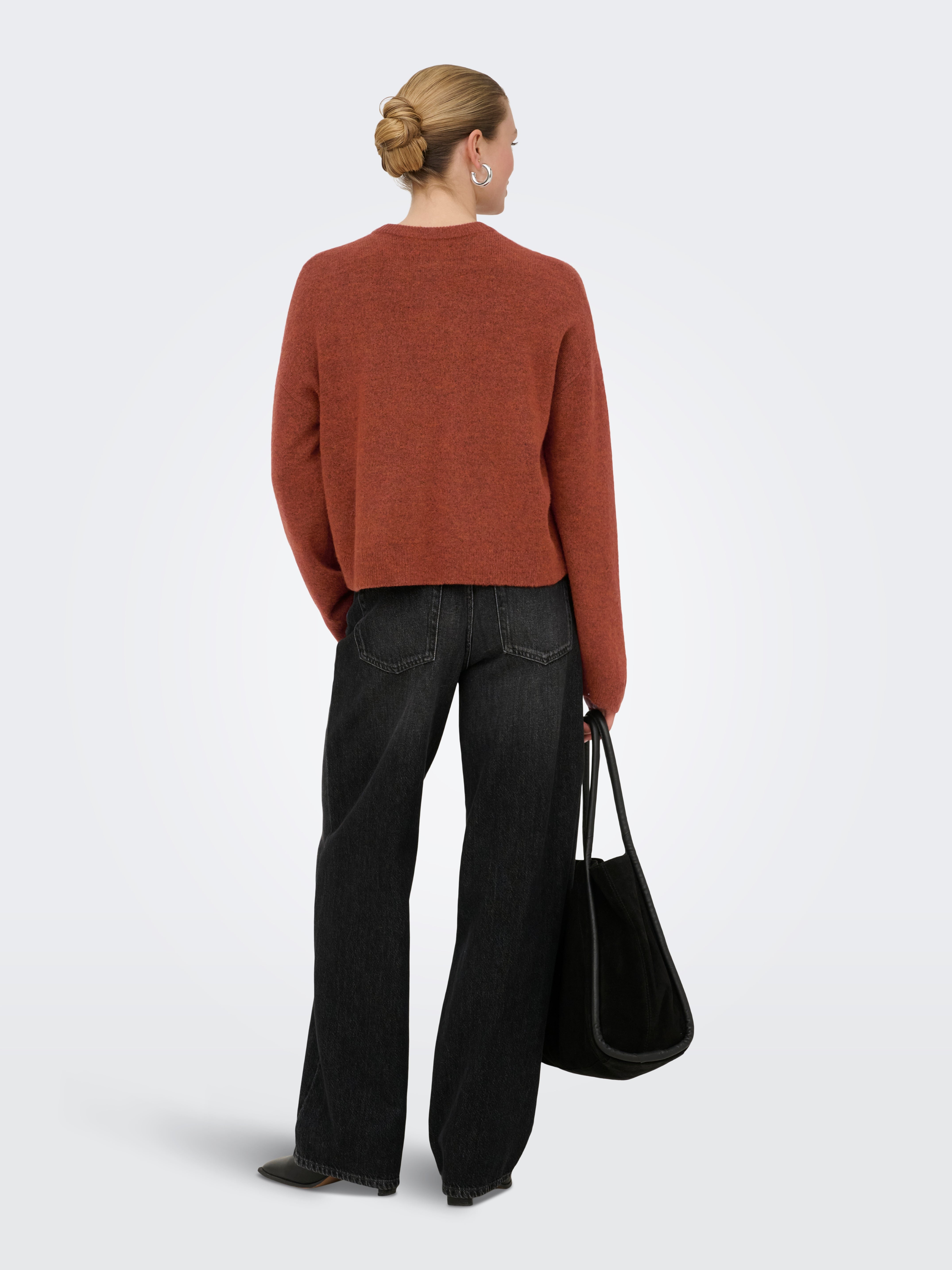 Back view of a rust-colored sweater paired with black wide-leg denim jeans and a black tote bag.