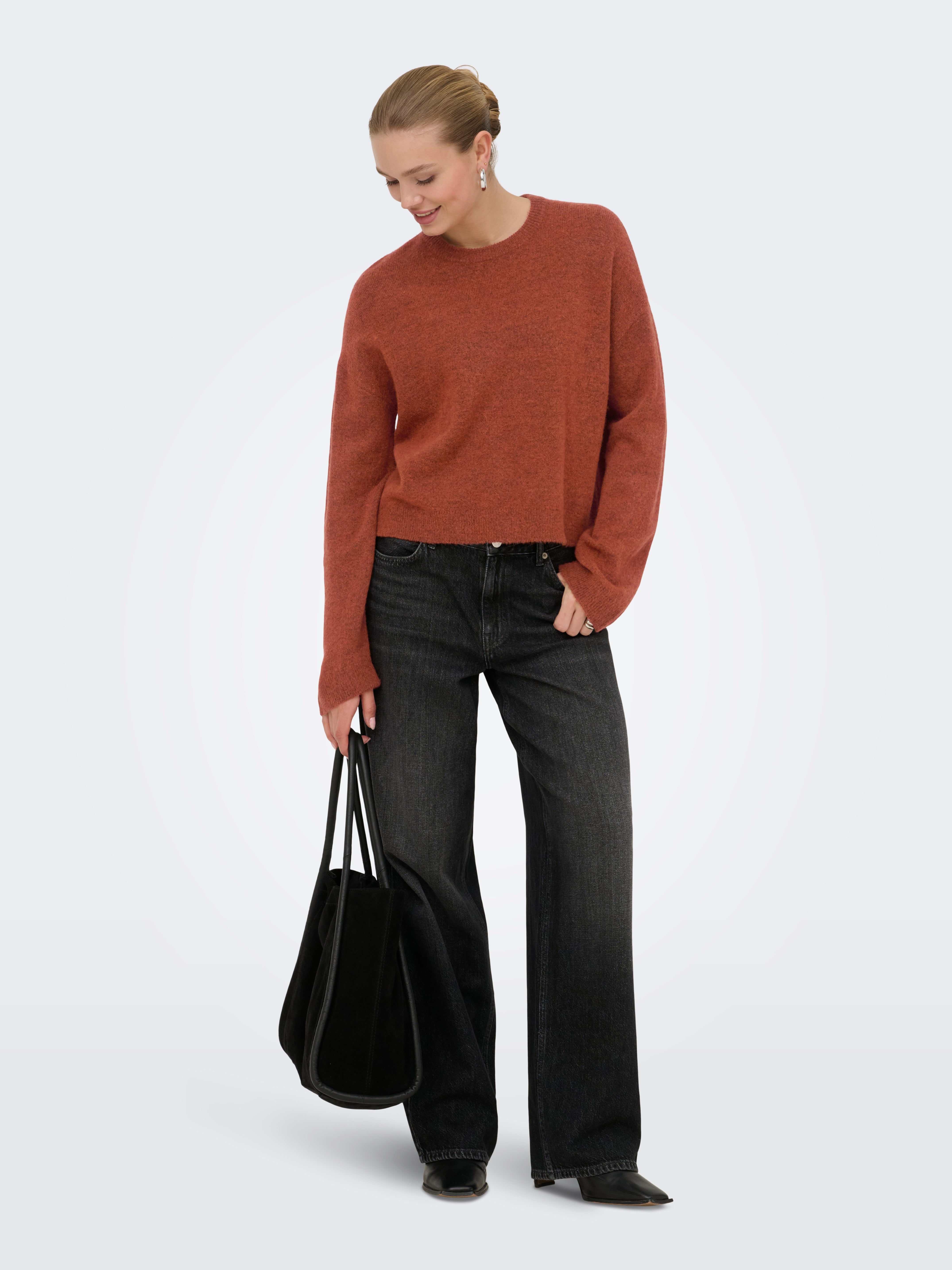 Slim-fit dark denim jeans paired with a rust-colored sweater and black tote bag on gray background.