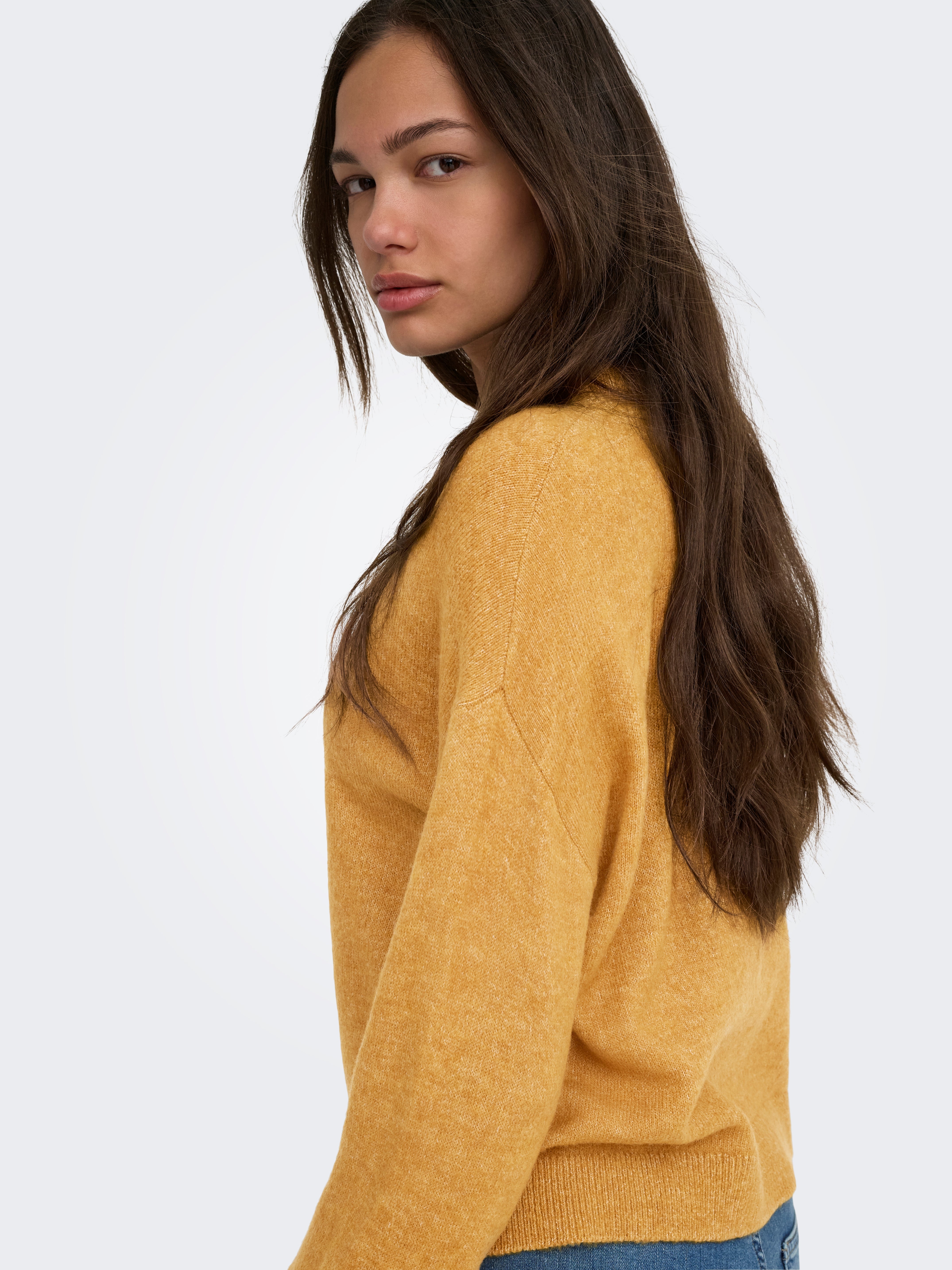 Side view of long dark hair and a mustard yellow sweater with ribbed cuffs and hem against a light background.