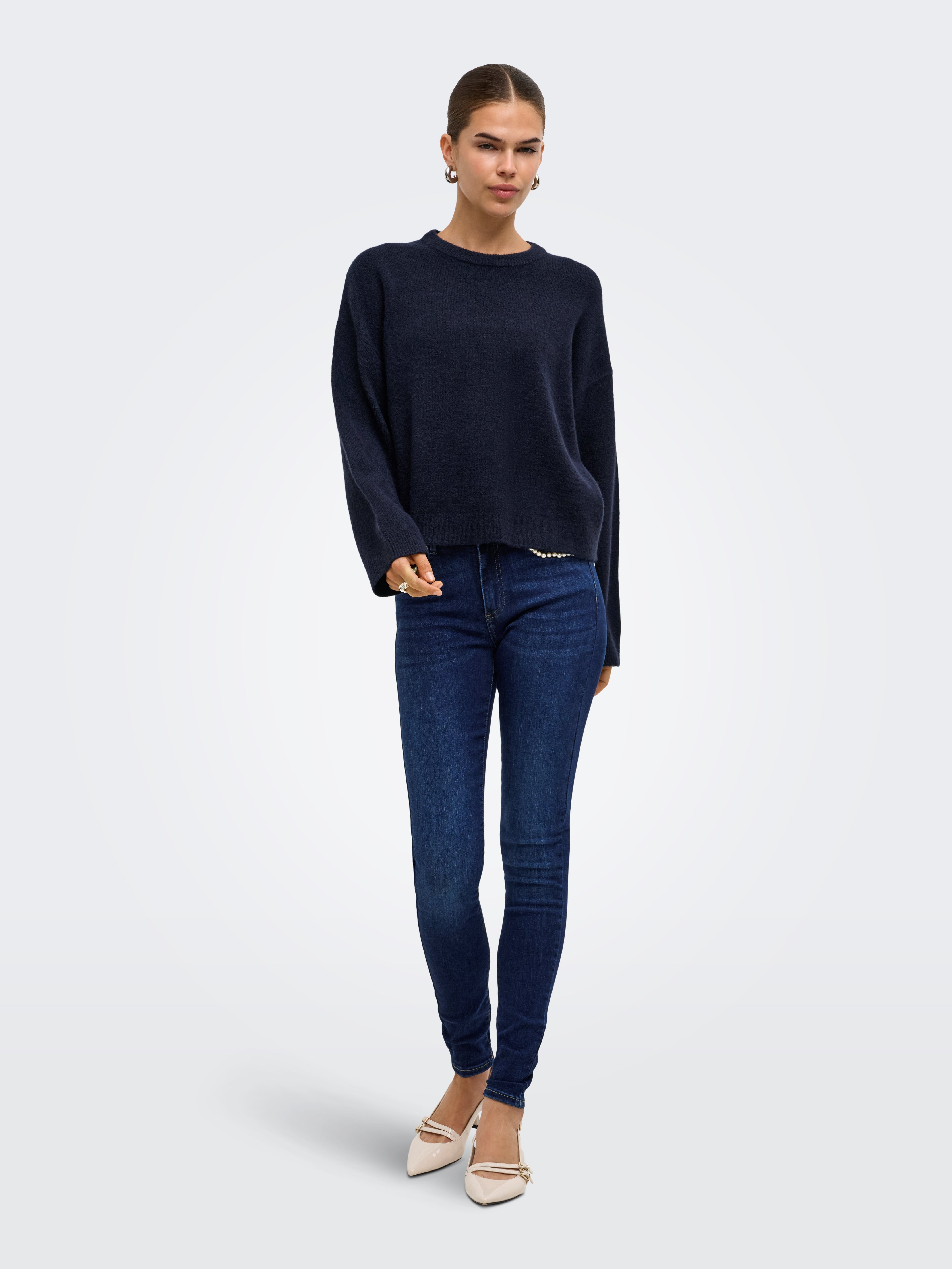 Navy blue sweater paired with dark blue skinny denim jeans and beige pointed-toe heels on a neutral background.