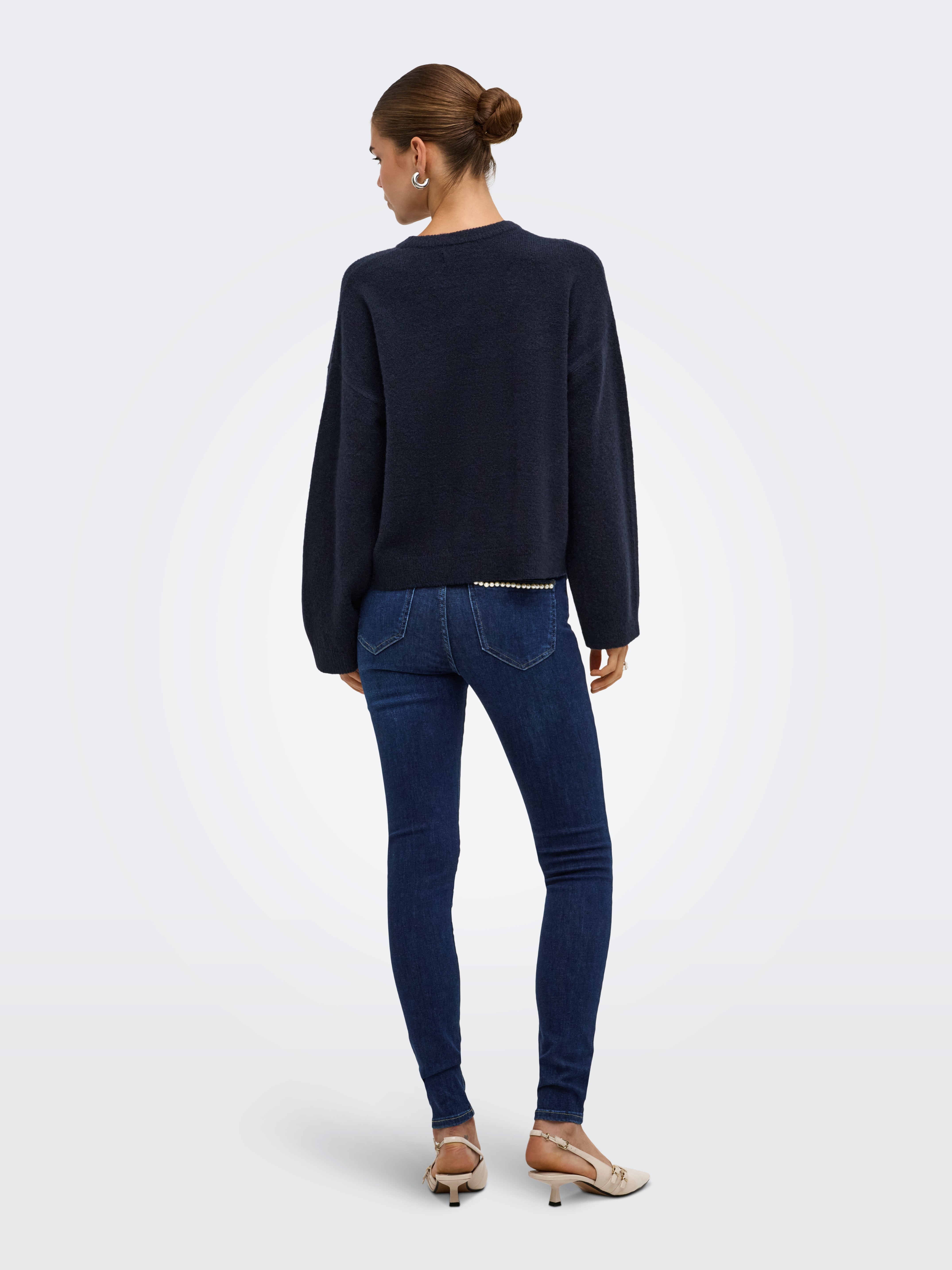 Back view of a navy sweater paired with dark blue denim skinny jeans and beige heels on a light background.