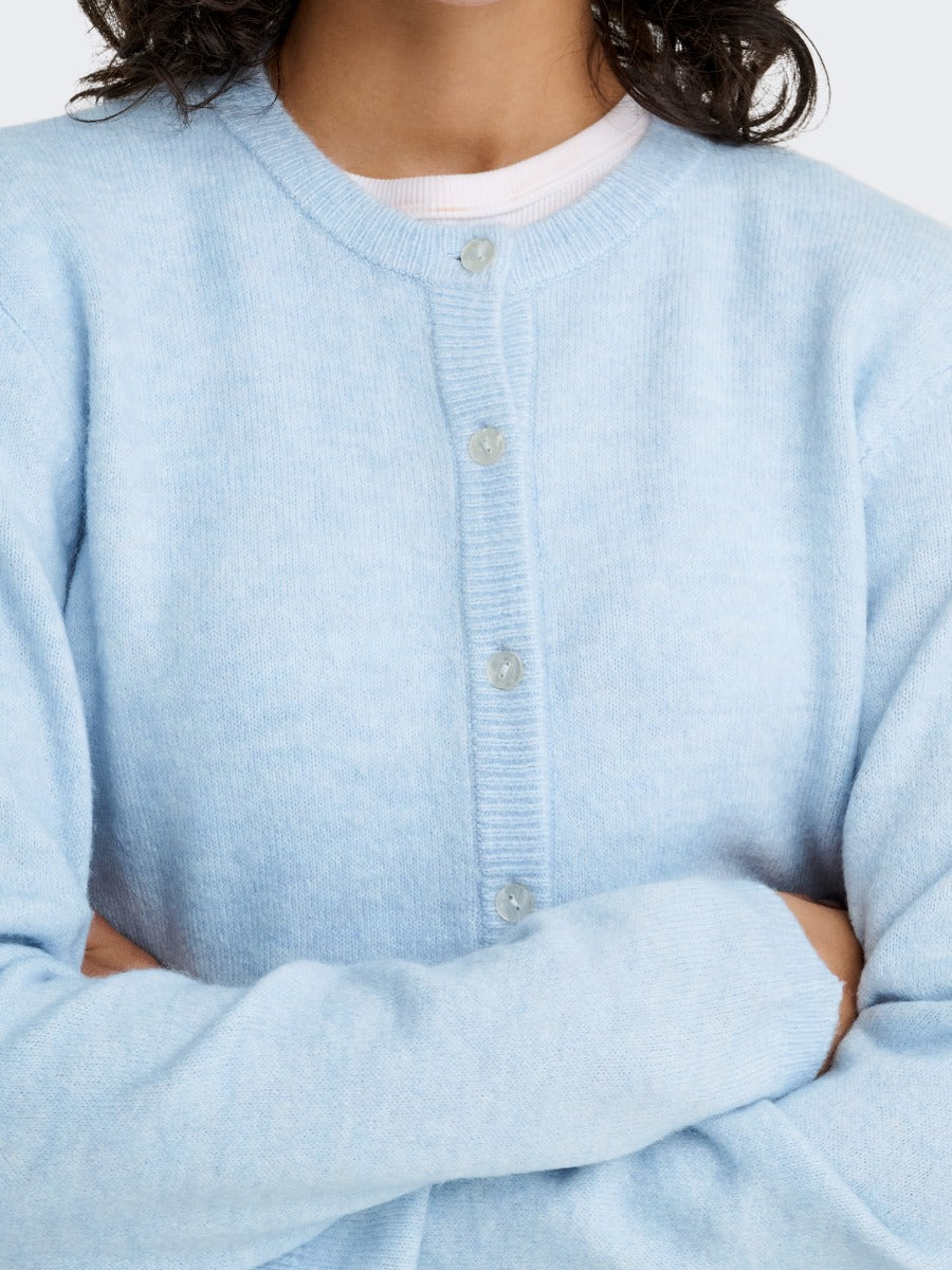 Light blue buttoned cardigan sweater worn over a white crew neck top with arms crossed.