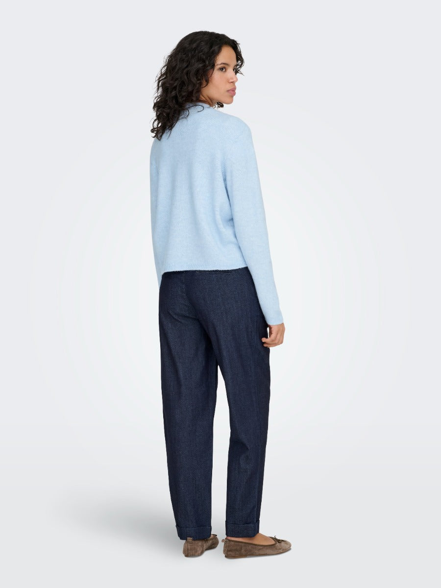 Person in a light blue sweater and dark denim pants standing with back facing the camera on plain background