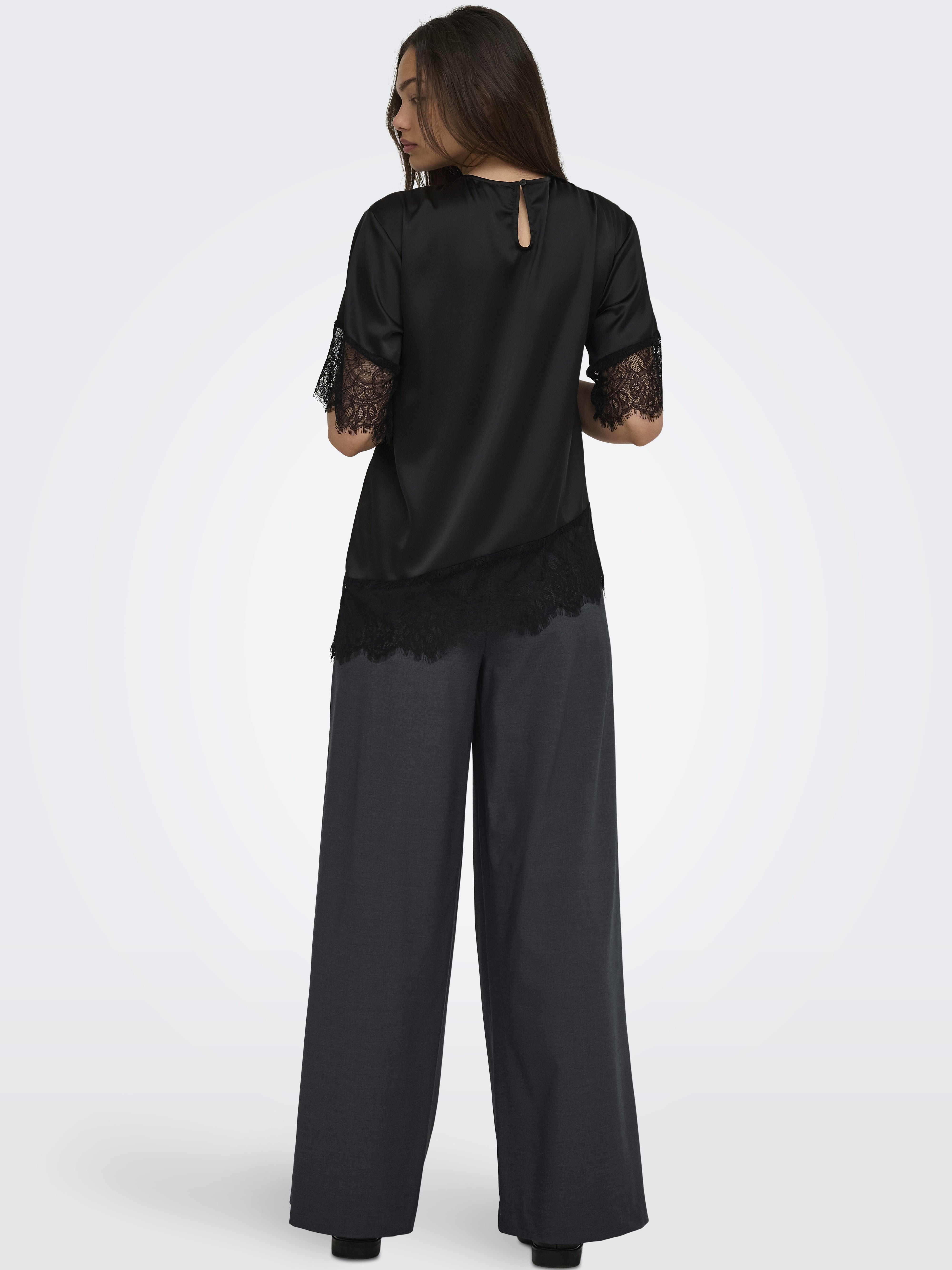 Back view of a black satin top with lace trim paired with loose dark wide-leg trousers on a neutral background.